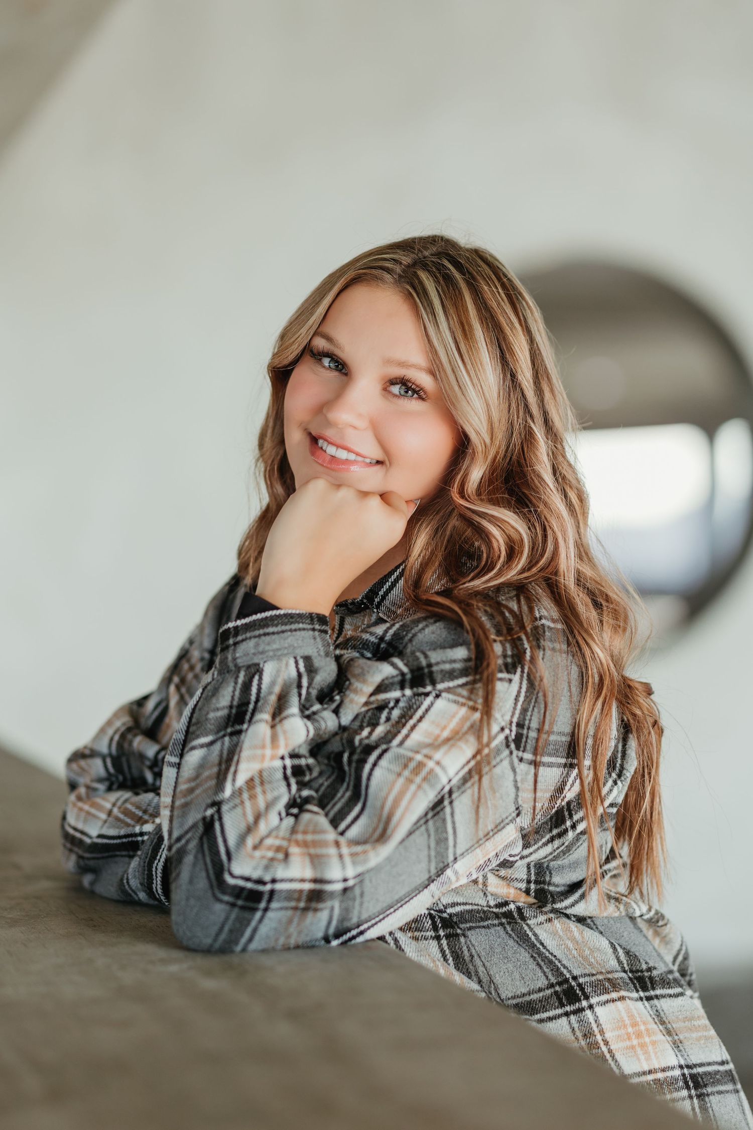 Indoor portrait wearing plaid flannel with styled wavy hair.