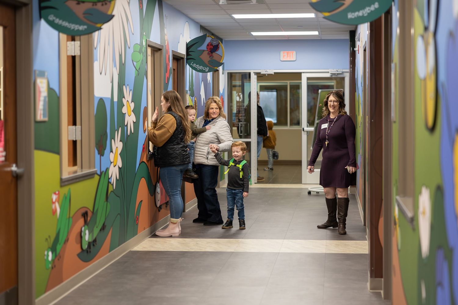 A corridor with colorful nature-themed wall murals and people gathered along the walls.