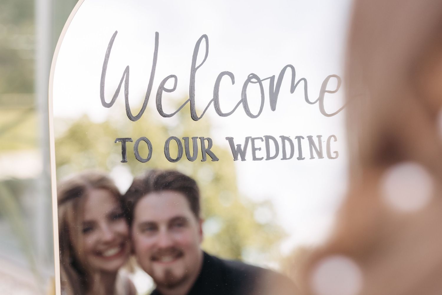 Welcome to our wedding sign with blurred couple in background.