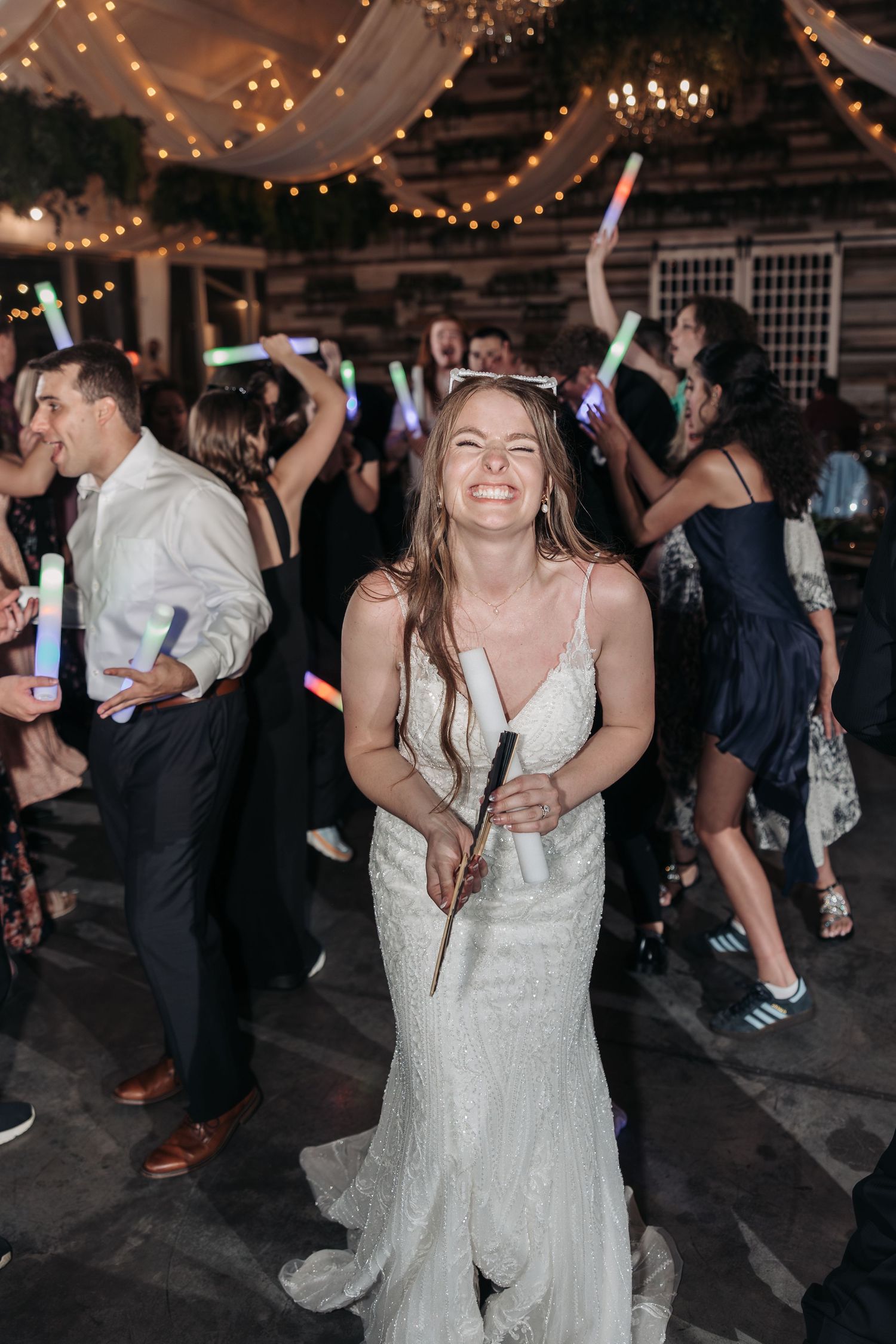 Reception celebration features dancing with illuminated wands under twinkling lights.