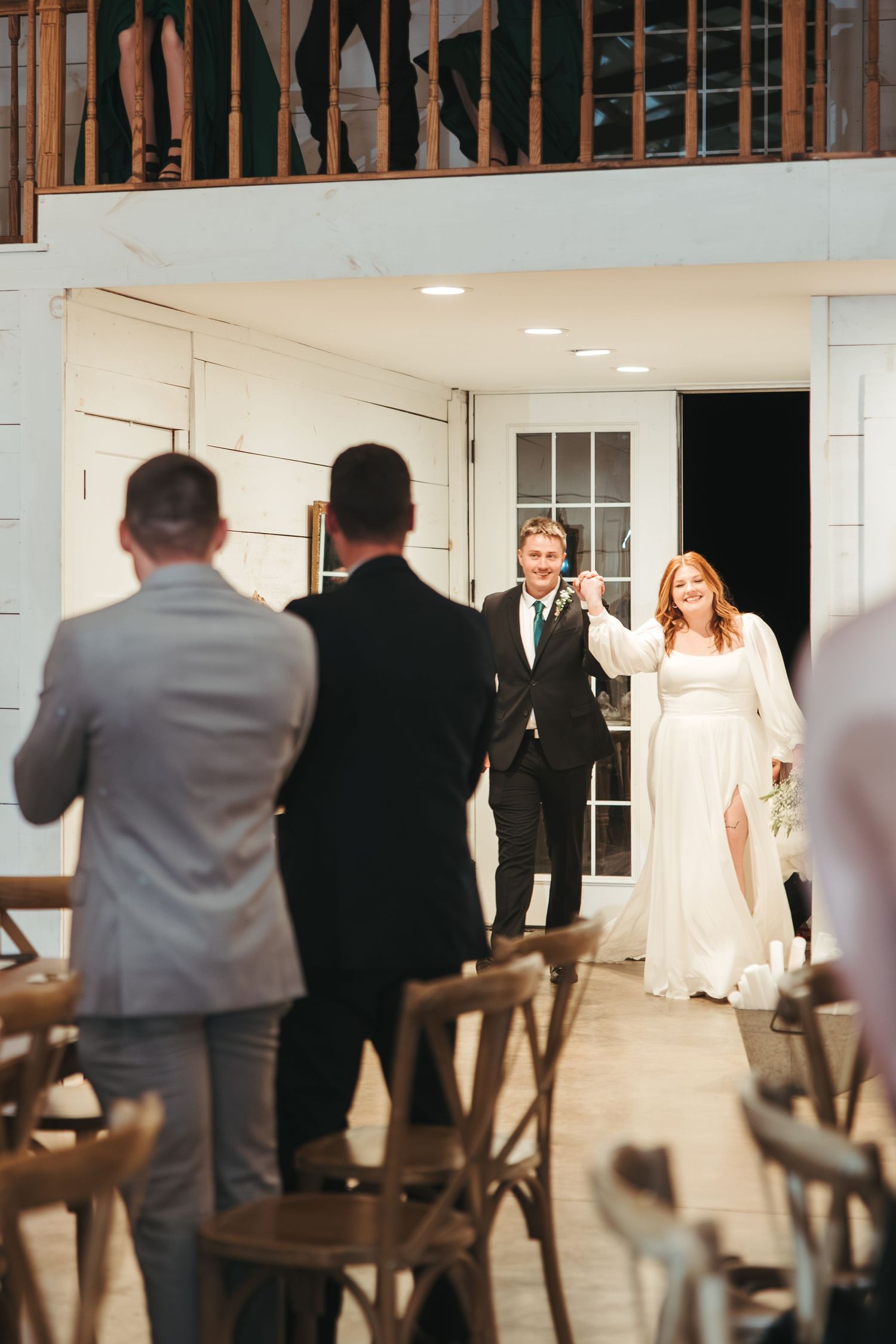 Wedding ceremony entrance in white indoor venue with wooden chairs.