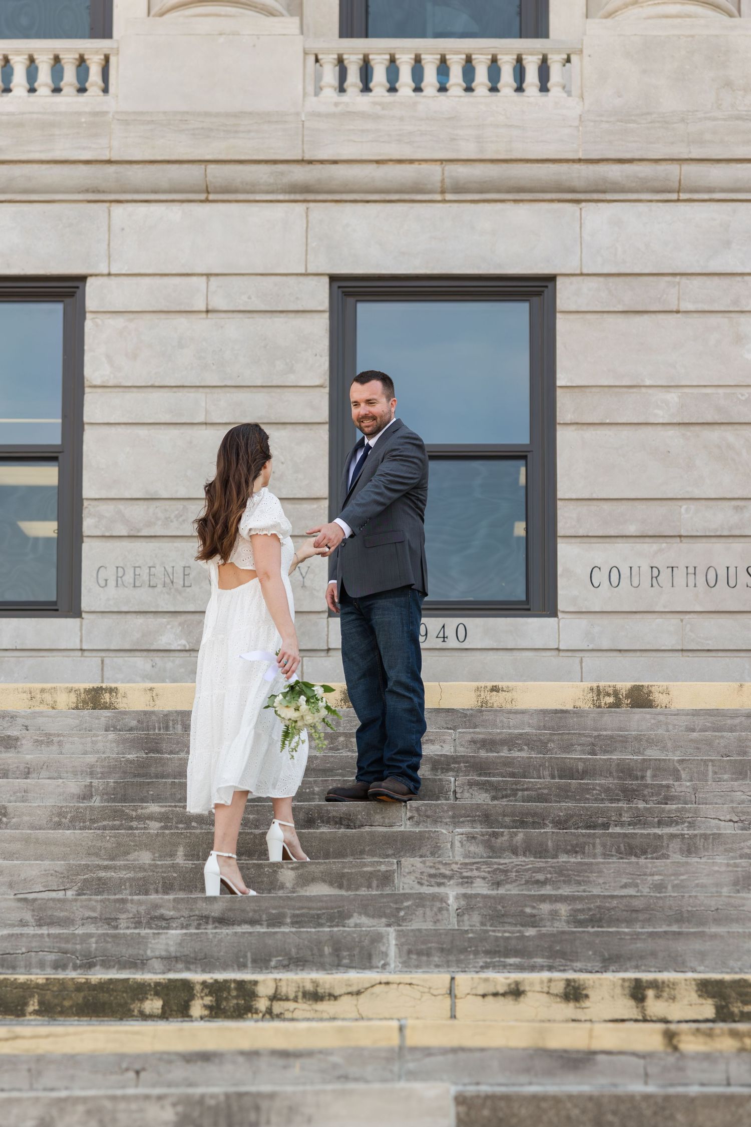 Couple in formal attire stands on courthouse steps for a wedding ceremony photo.