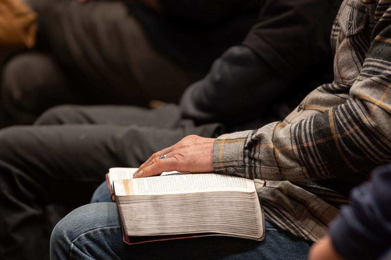 Person in casual clothing holds large white book while sitting, focused on reading in dim lighting.