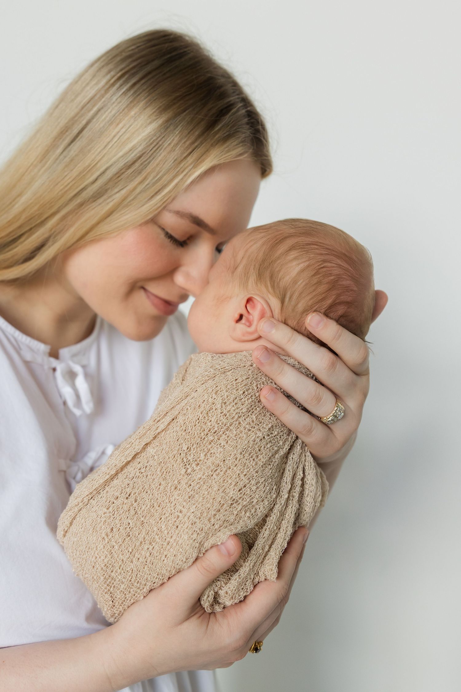 A tender moment between parent and baby in soft beige tones against a white background.