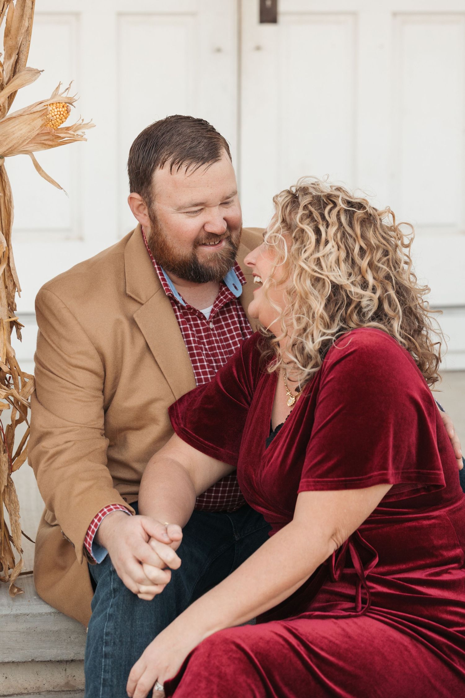 Couple sharing intimate moment on white porch steps with fall decorations.