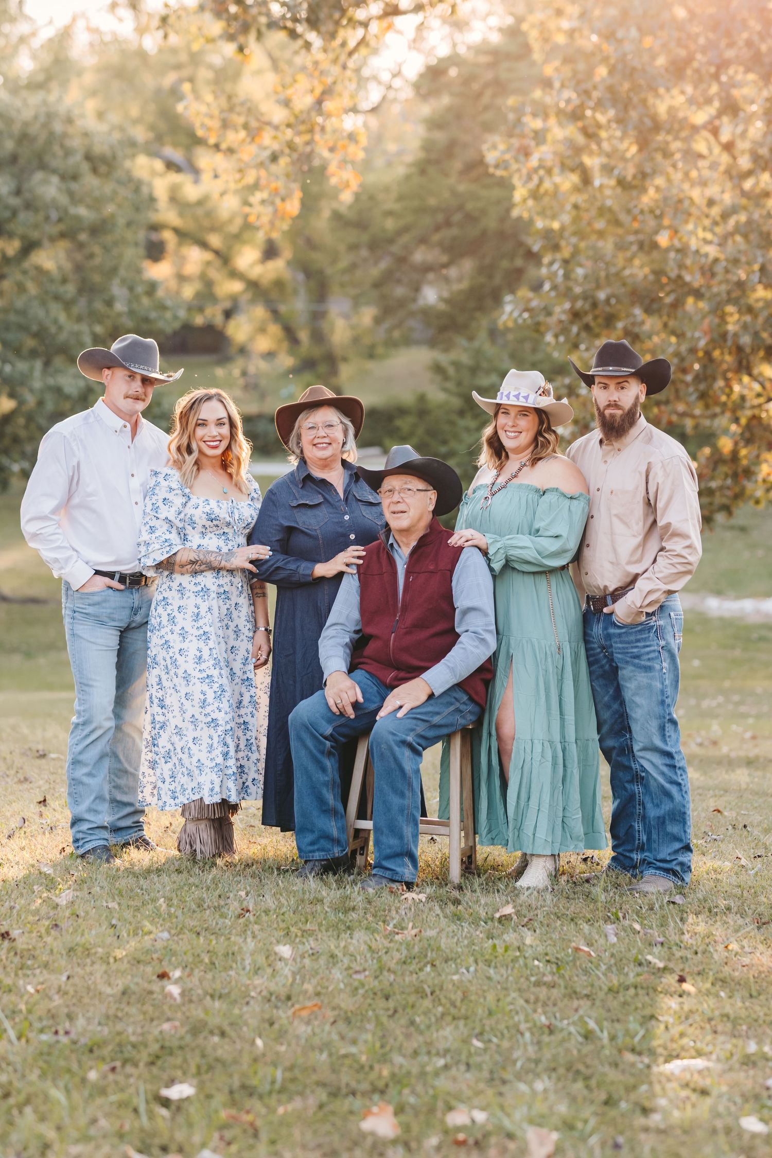 Extended family in coordinated western outfits poses for portrait in natural outdoor setting.