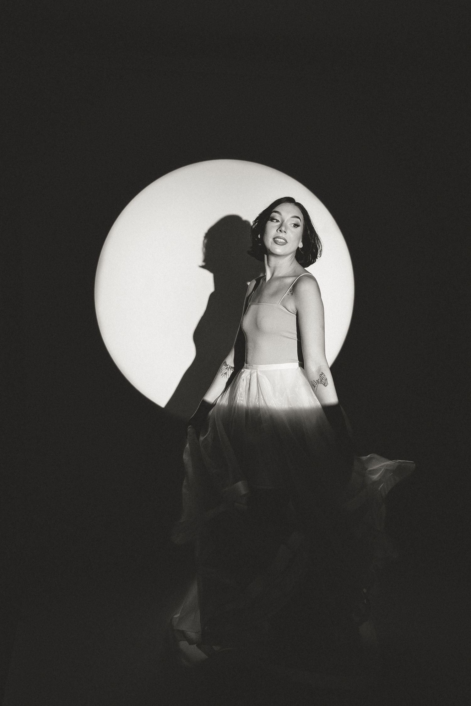 Artistic black and white portrait of a figure against a circular light backdrop.