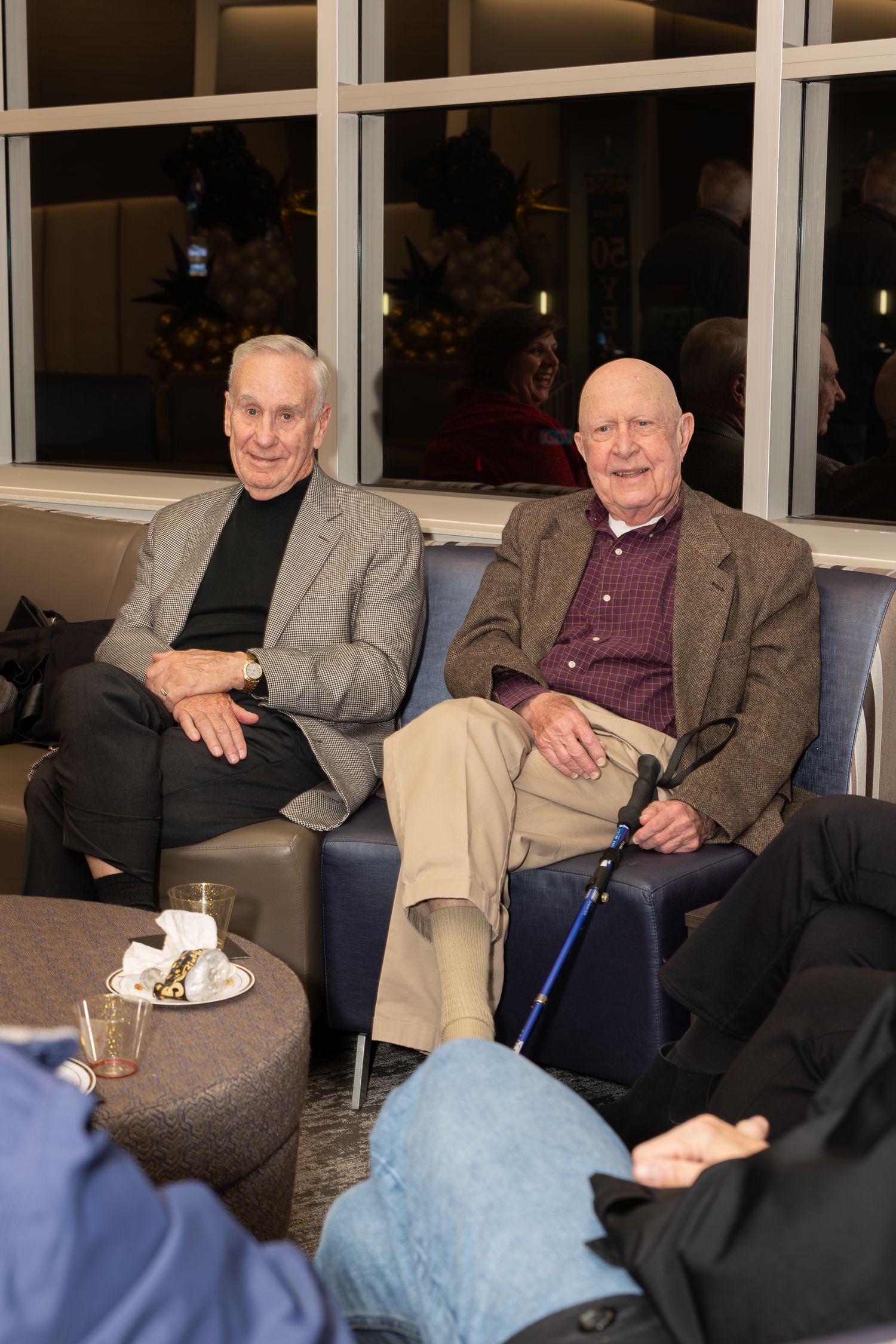 Two senior guests seated on blue couch at corporate celebration event.