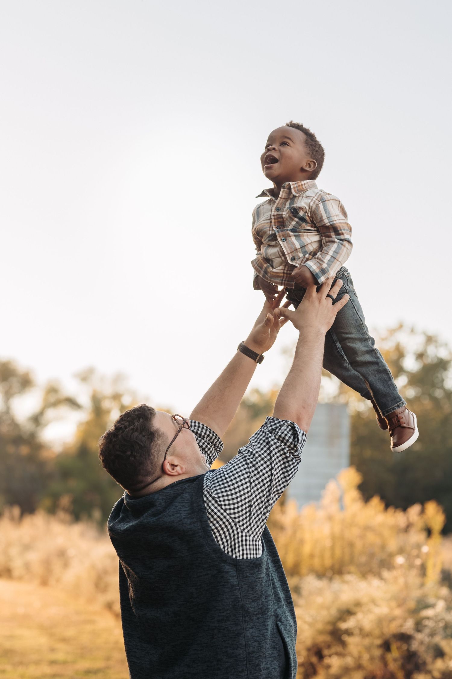 A joyful moment captured as an adult lifts a child high into the air against a golden sunset background.