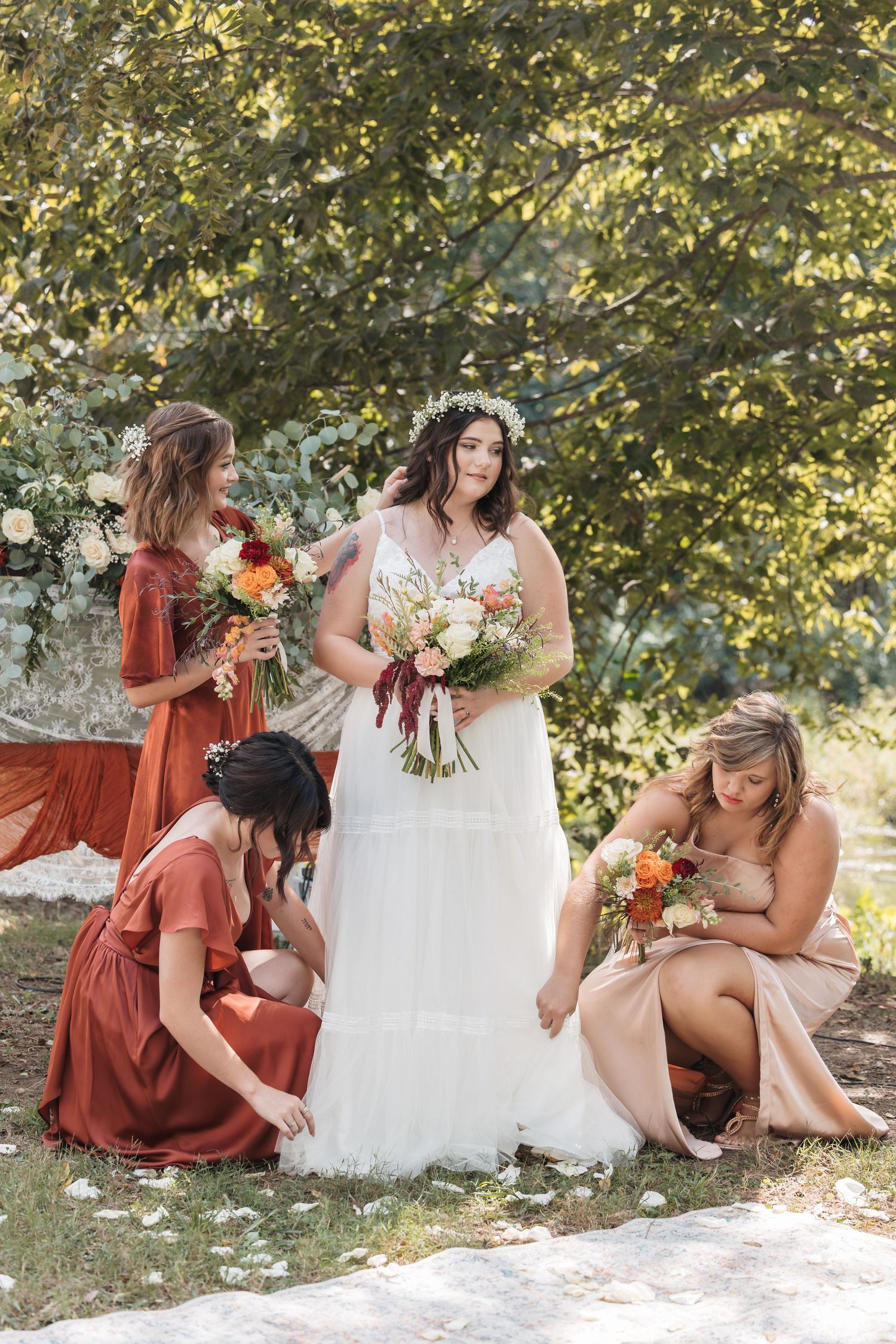 A bridal party in rust-colored dresses gathers outdoors with bouquets featuring autumn-toned flowers.
