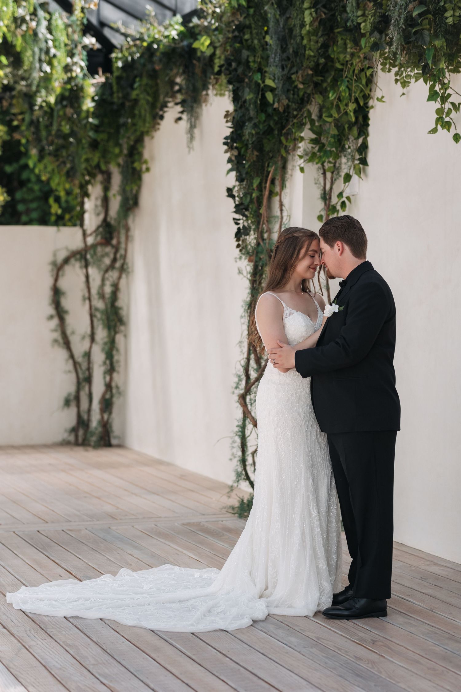 Romantic wedding portrait against white wall with cascading ivy and wooden deck.
