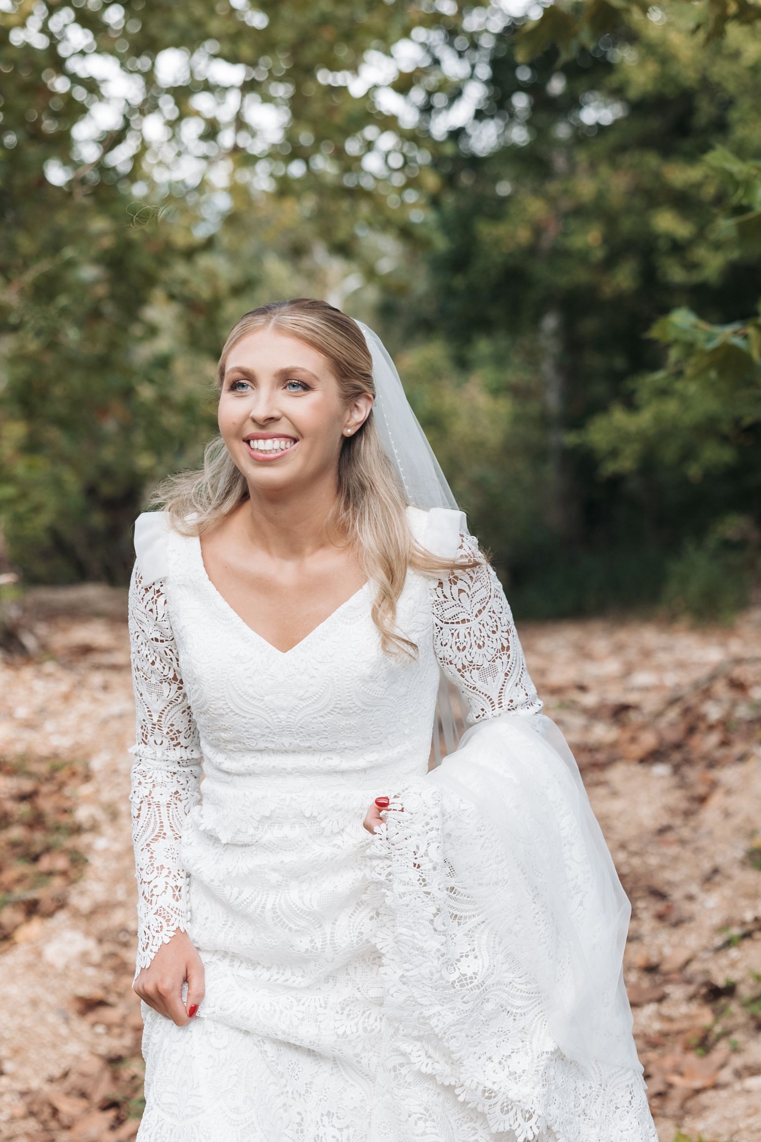A bride in a long-sleeve lace wedding dress and veil poses outdoors on her wedding day.