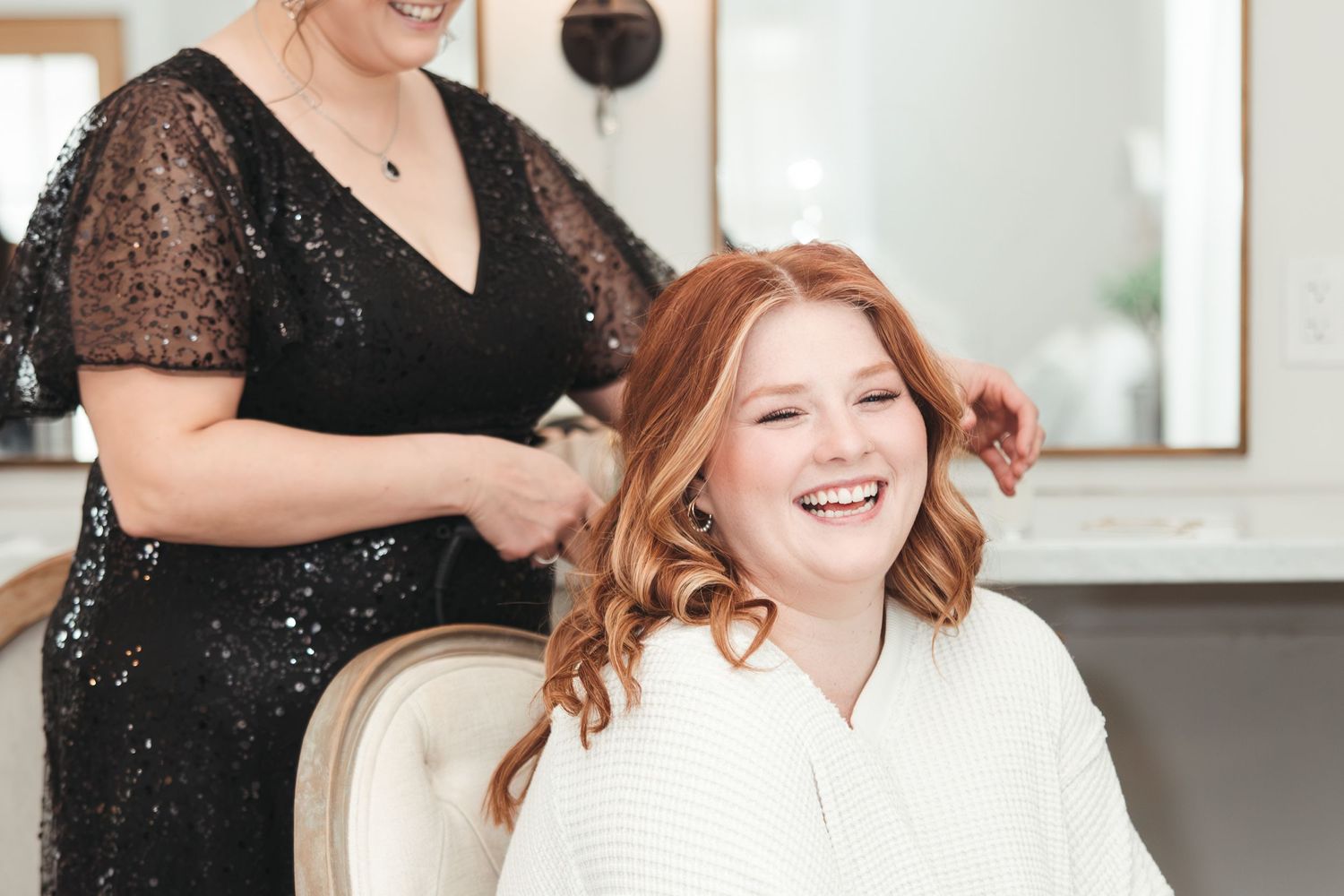Hairstylist in black sequined dress styling red hair during wedding preparation.