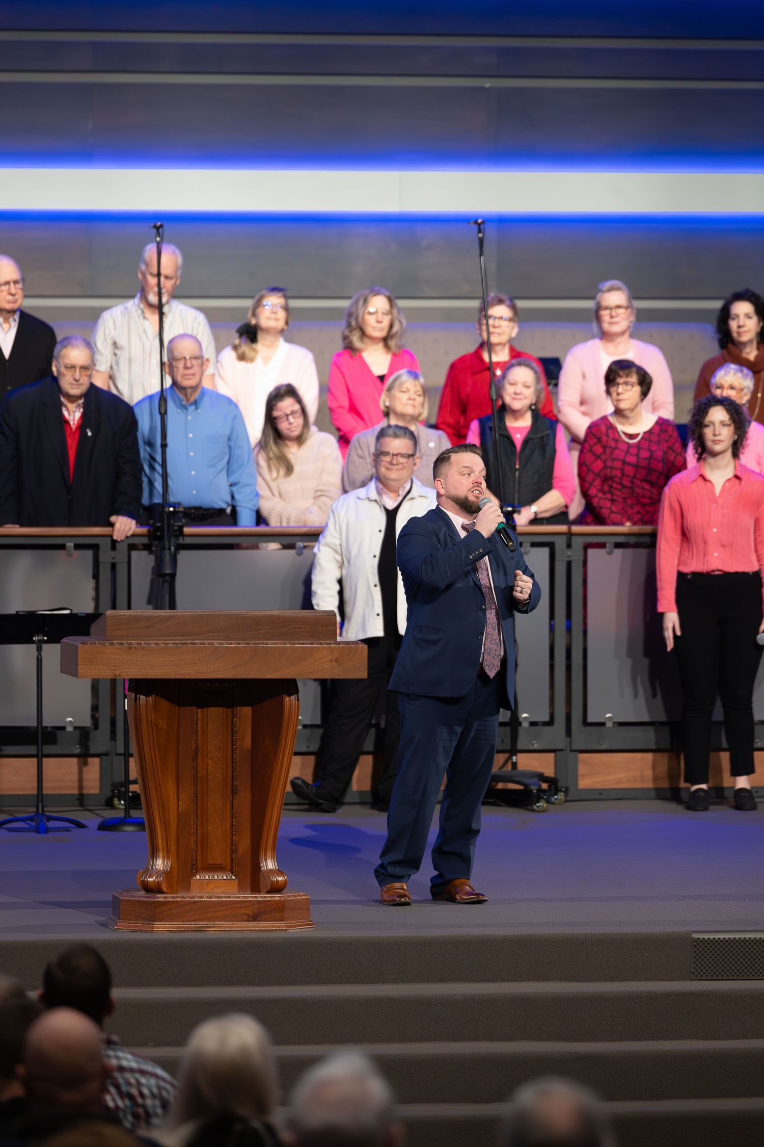 Church choir performing on stage with wooden podium and blue accent lighting.