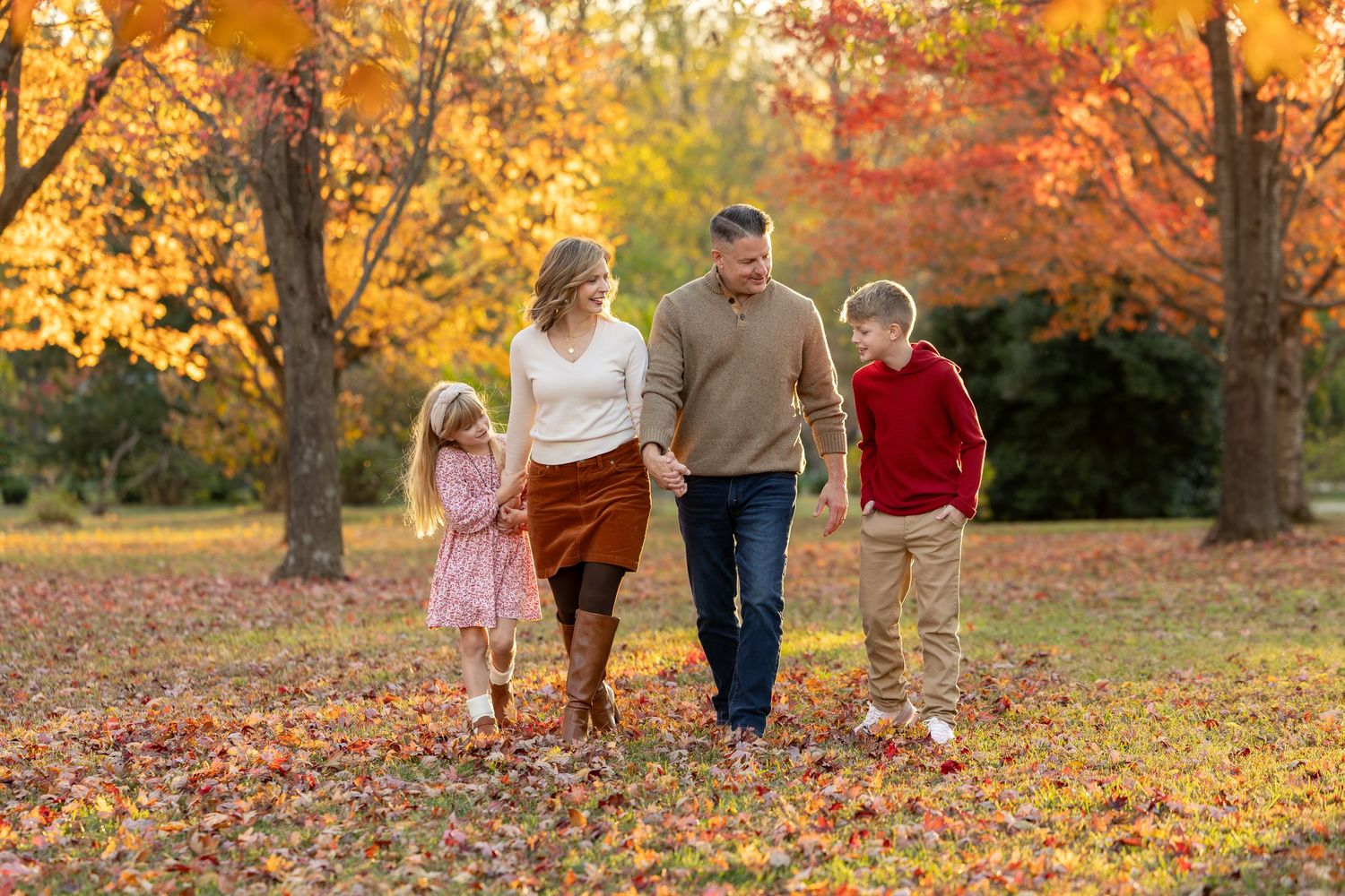 Family walking together through vibrant autumn foliage in a park during golden hour sunset.
