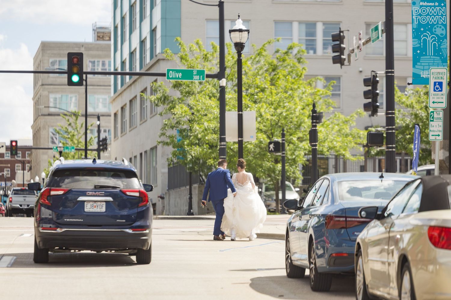 Bride and groom walk hand in hand across urban downtown street intersection on wedding day.