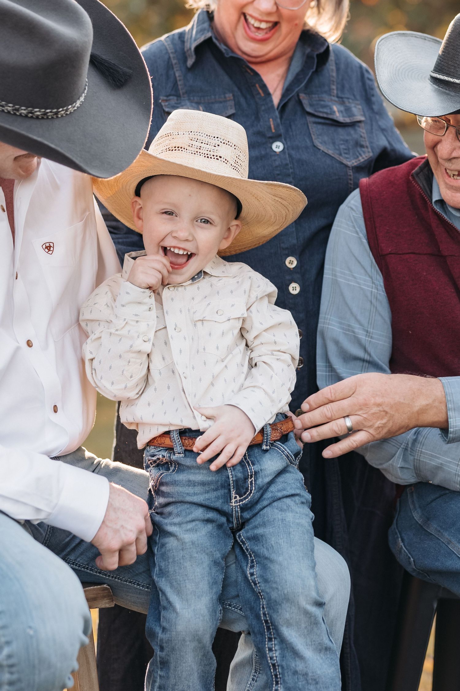 Young boy in cowboy hat and western wear laughs during family photo session.