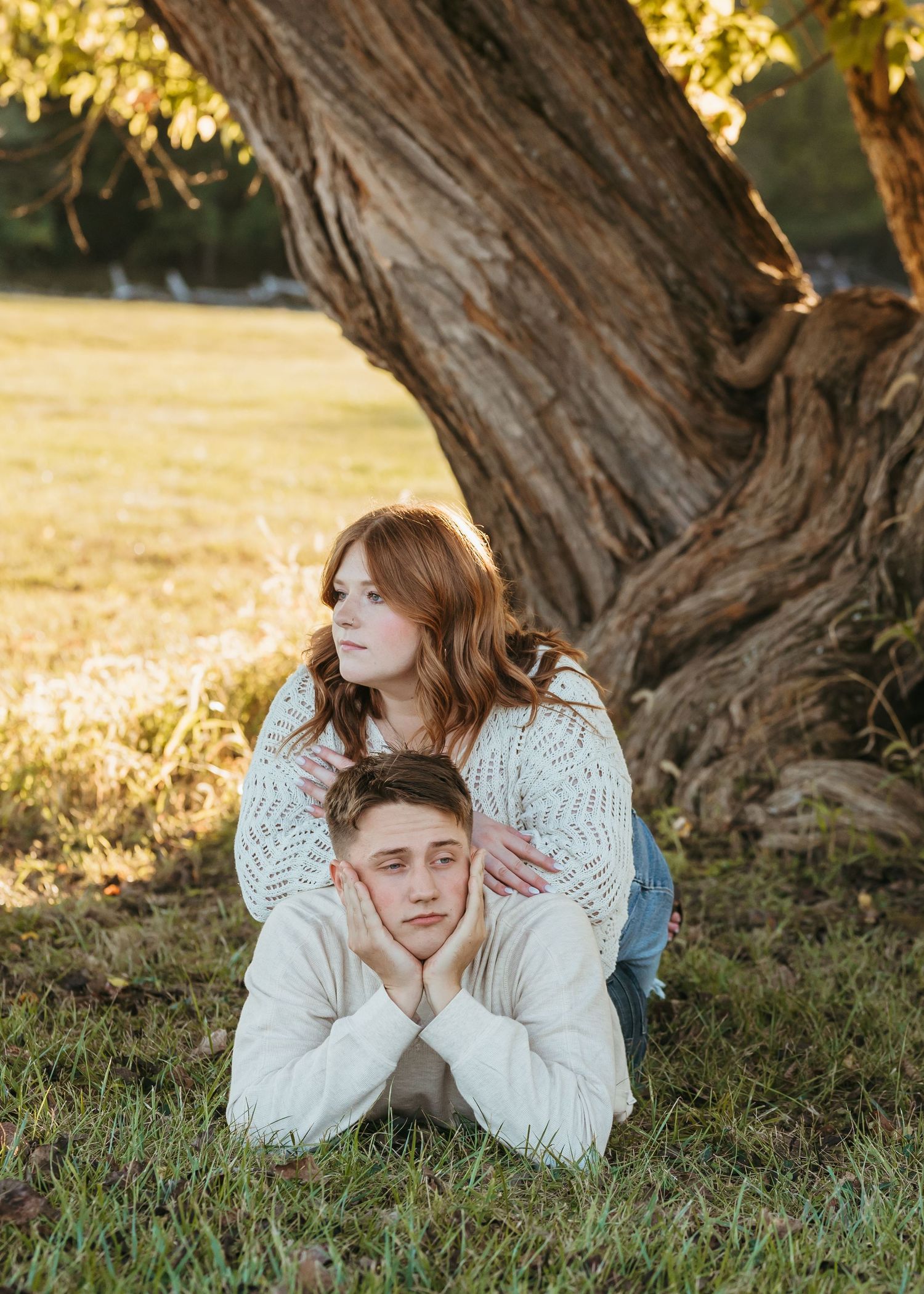Two people stacked on top of each other making funny faces by a tree trunk.