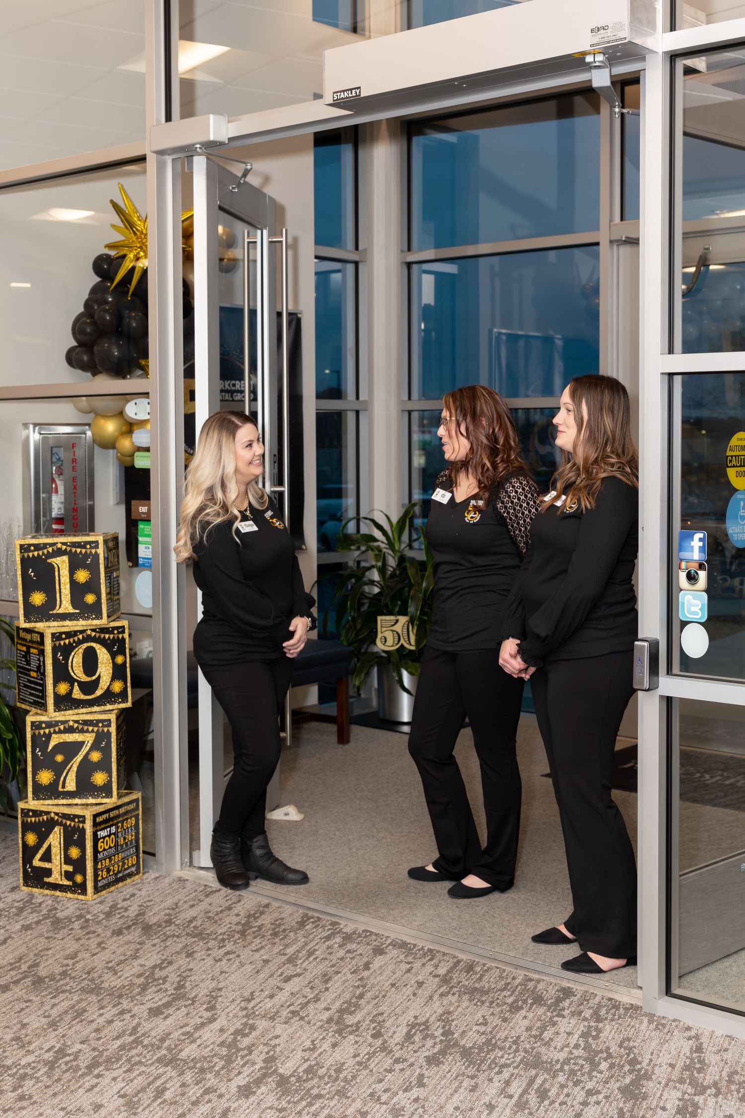 Three people in black attire having a conversation near decorative numbered blocks in an office entrance.