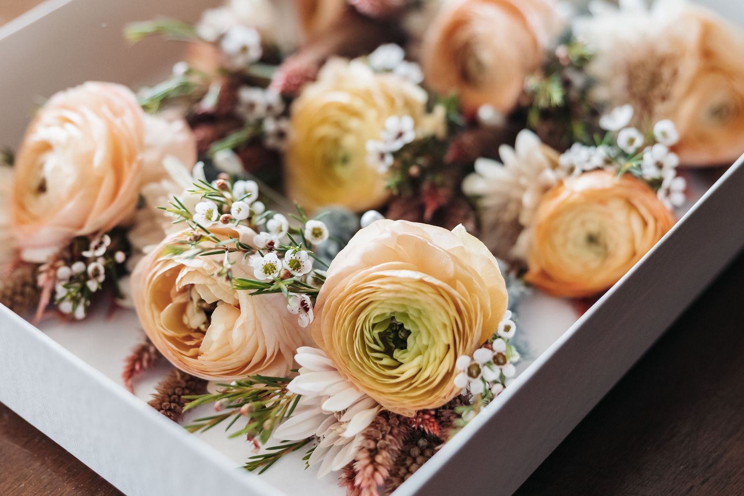 Delicate arrangement of peach ranunculus and baby's breath flowers in a box.