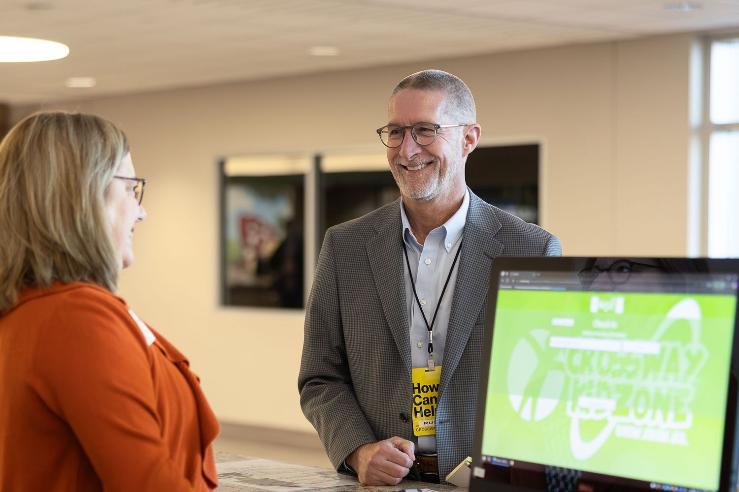 Two people having a friendly interaction at a registration desk with computer monitors.