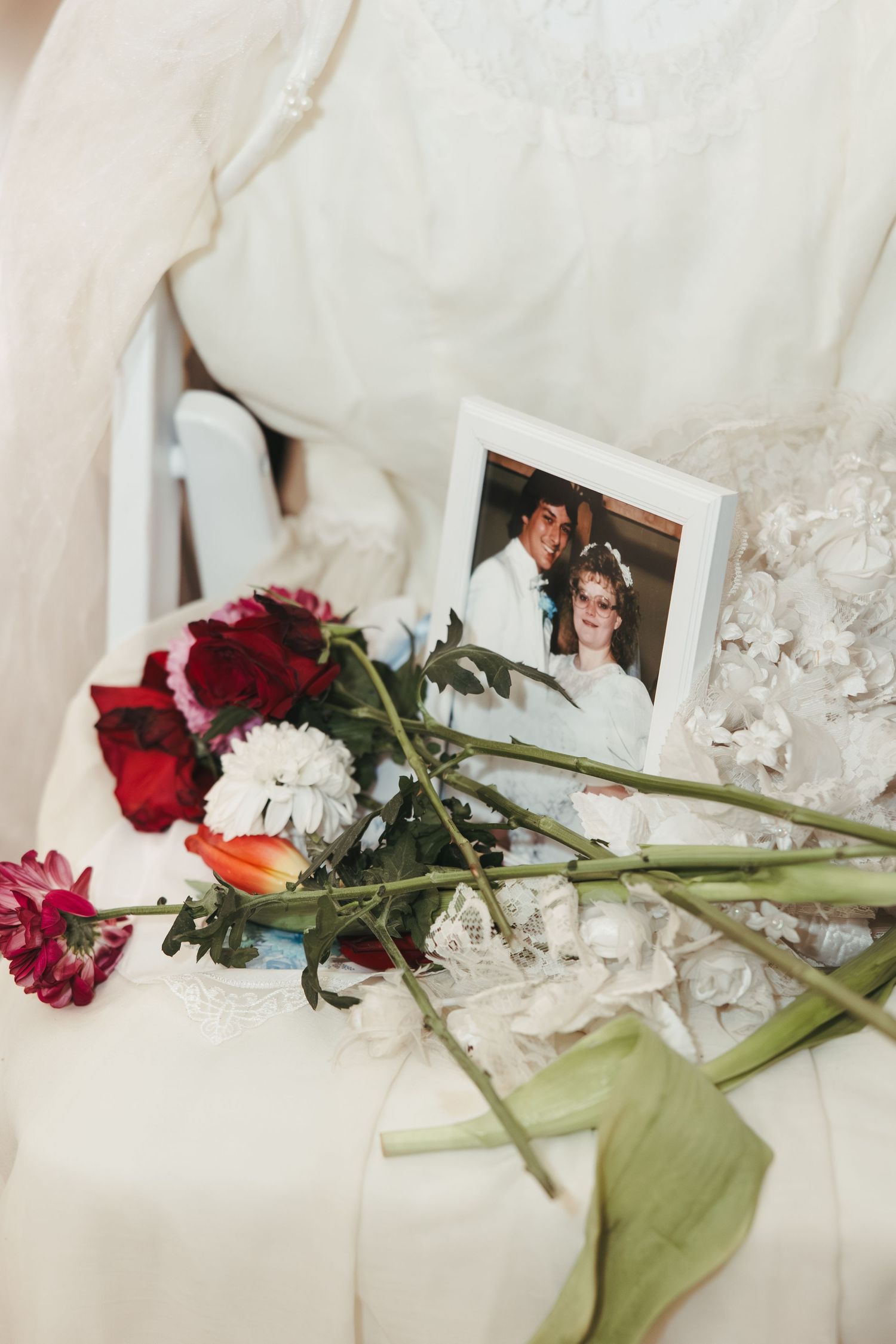 Red roses and a wedding photo lay on white fabric with delicate lace details.