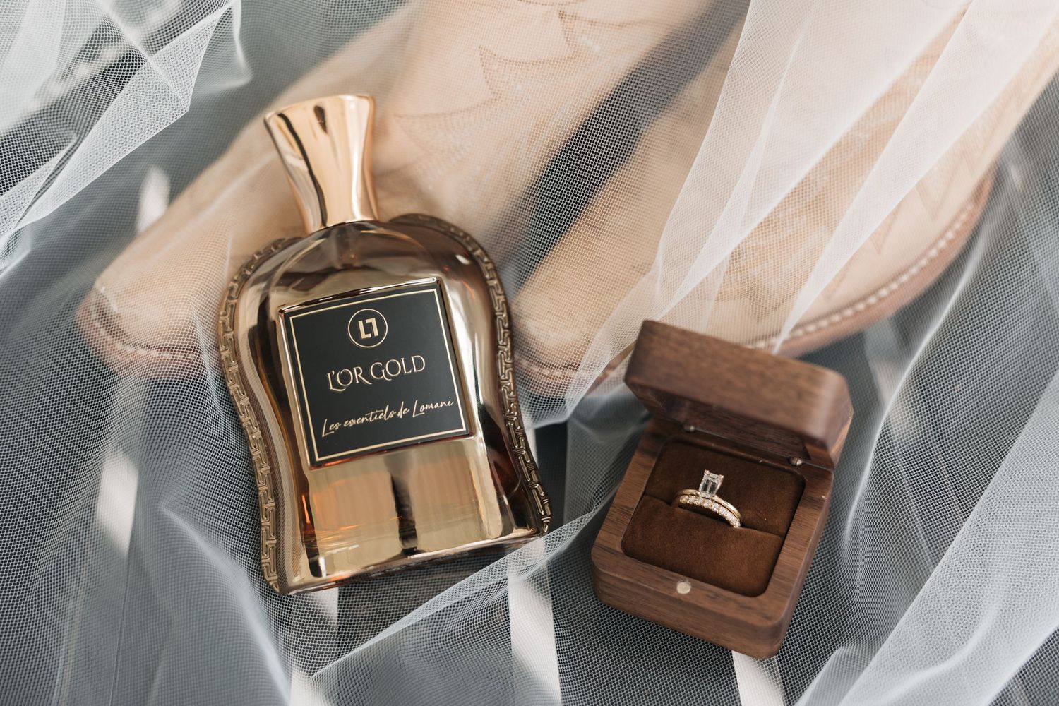 Perfume bottle and ring box arranged with wedding veil on gray fabric.