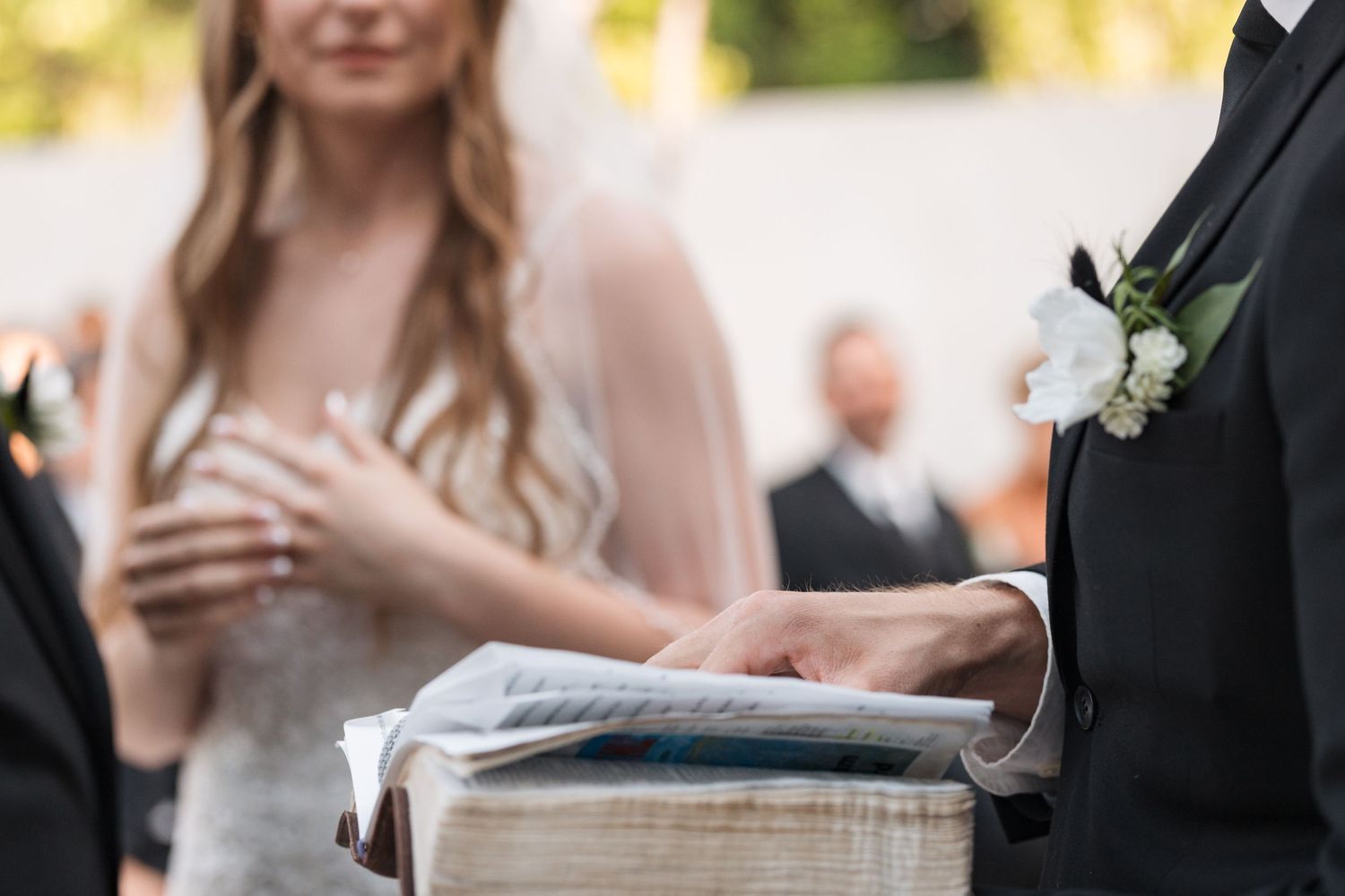 Close-up of hands during wedding ceremony with Bible in foreground.