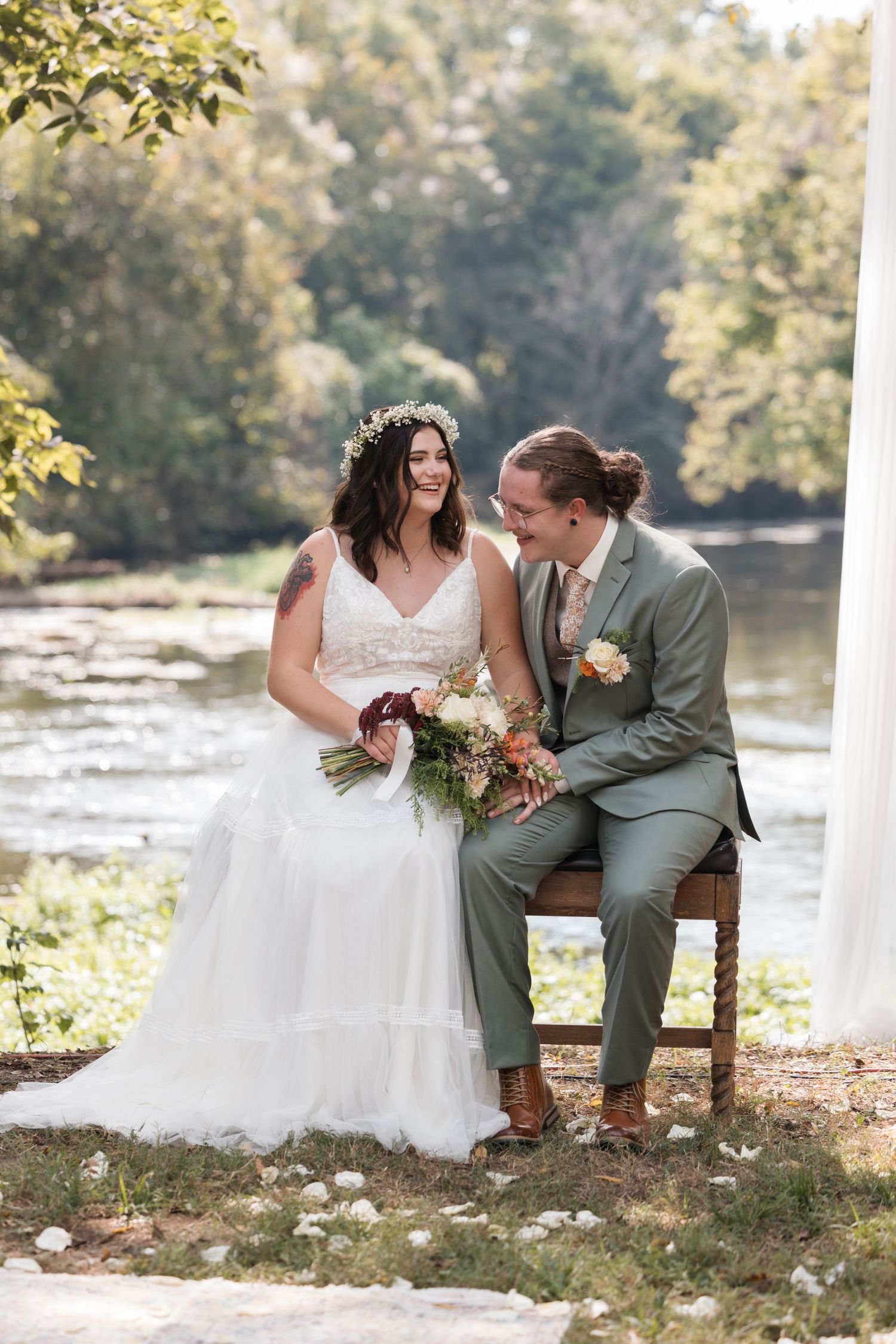 Couple sitting together by a river during their outdoor wedding ceremony.