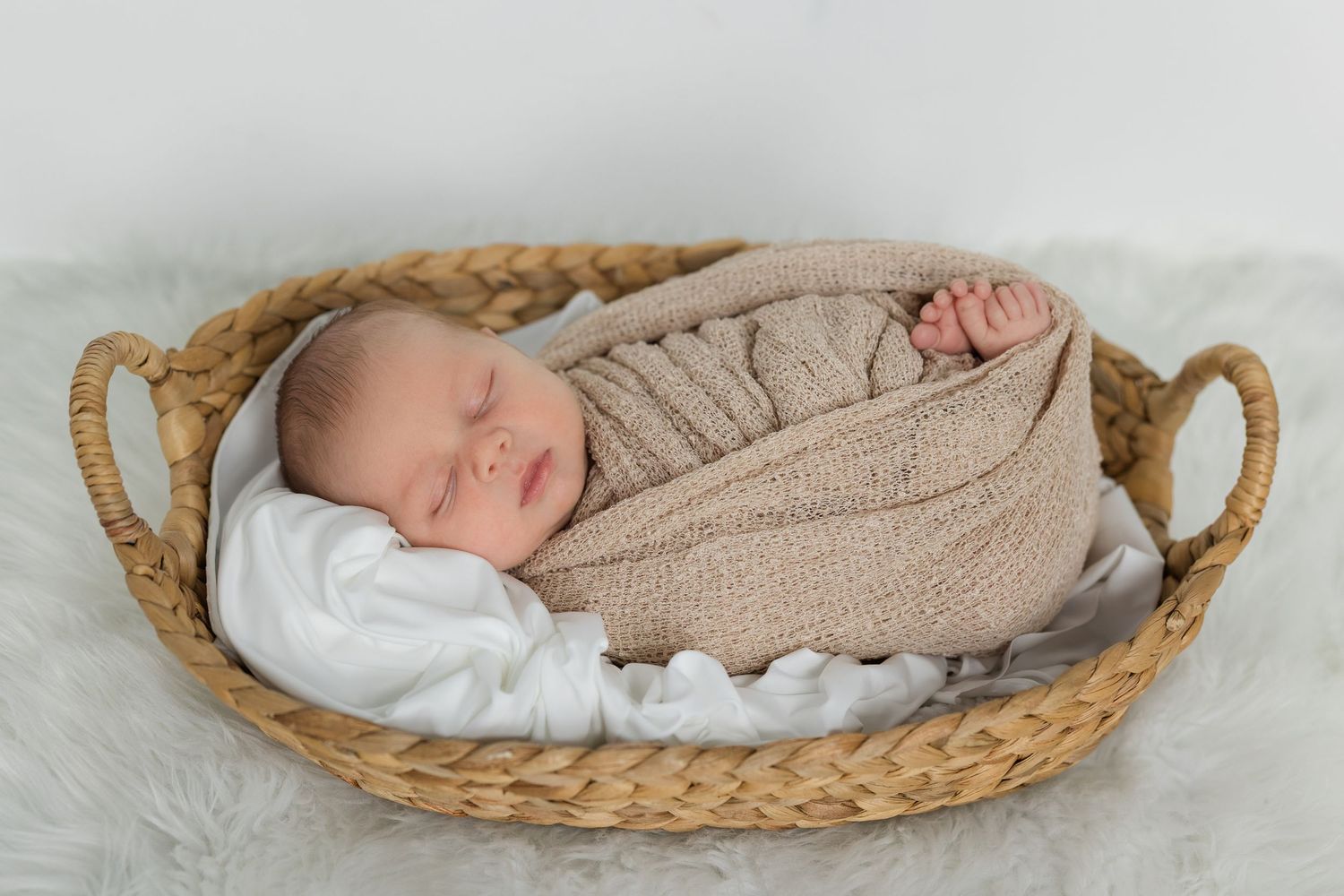 A sleeping newborn swaddled in a cozy knit blanket rests peacefully in a woven basket.