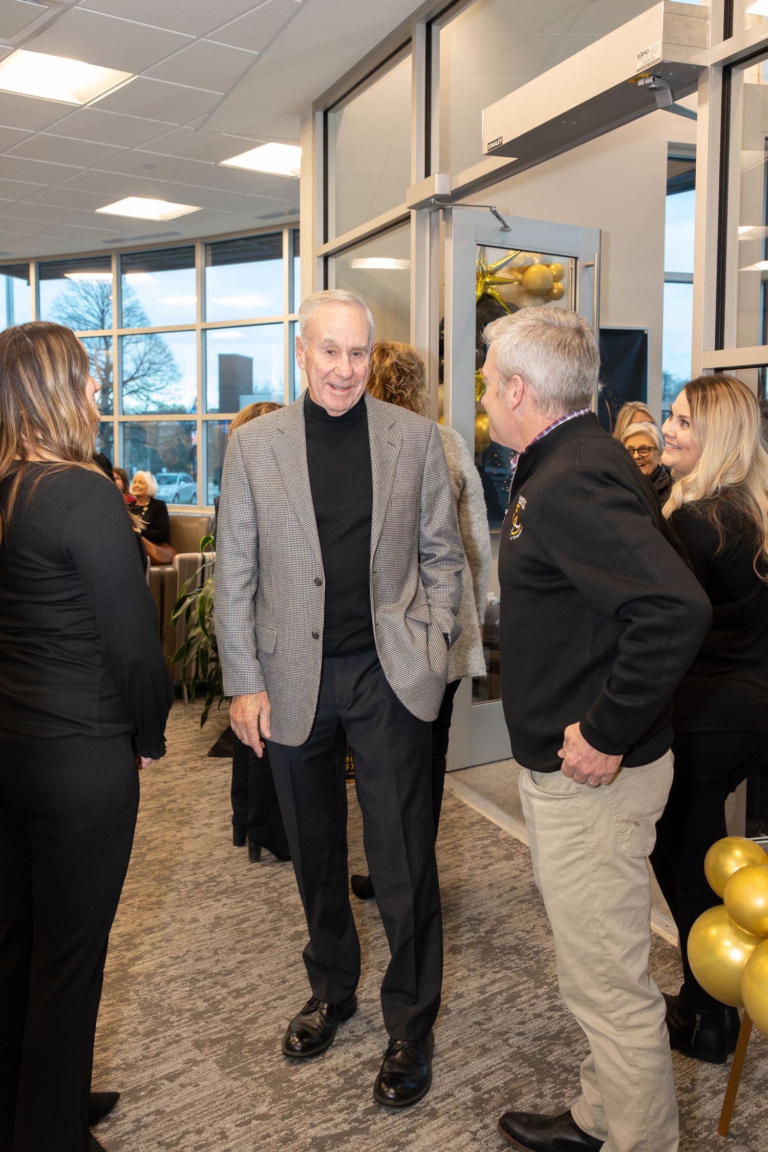 Professional gathering in office space with formal attire and gold balloon decorations.