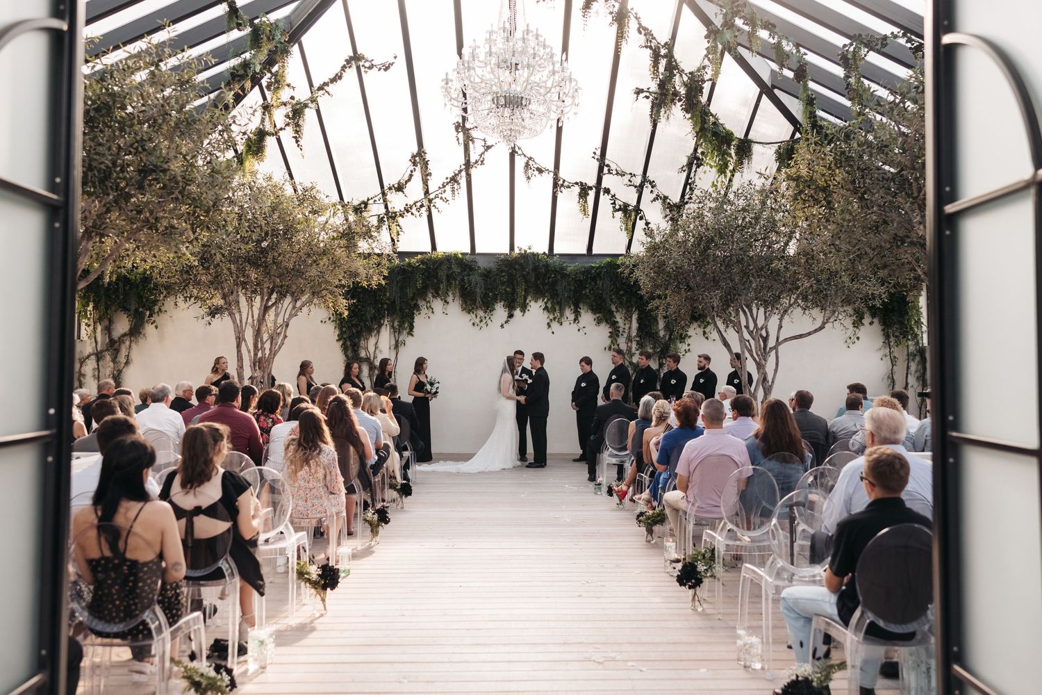 Wedding ceremony setup in an elegant glass-roofed venue with white aisle and floral decorations.
