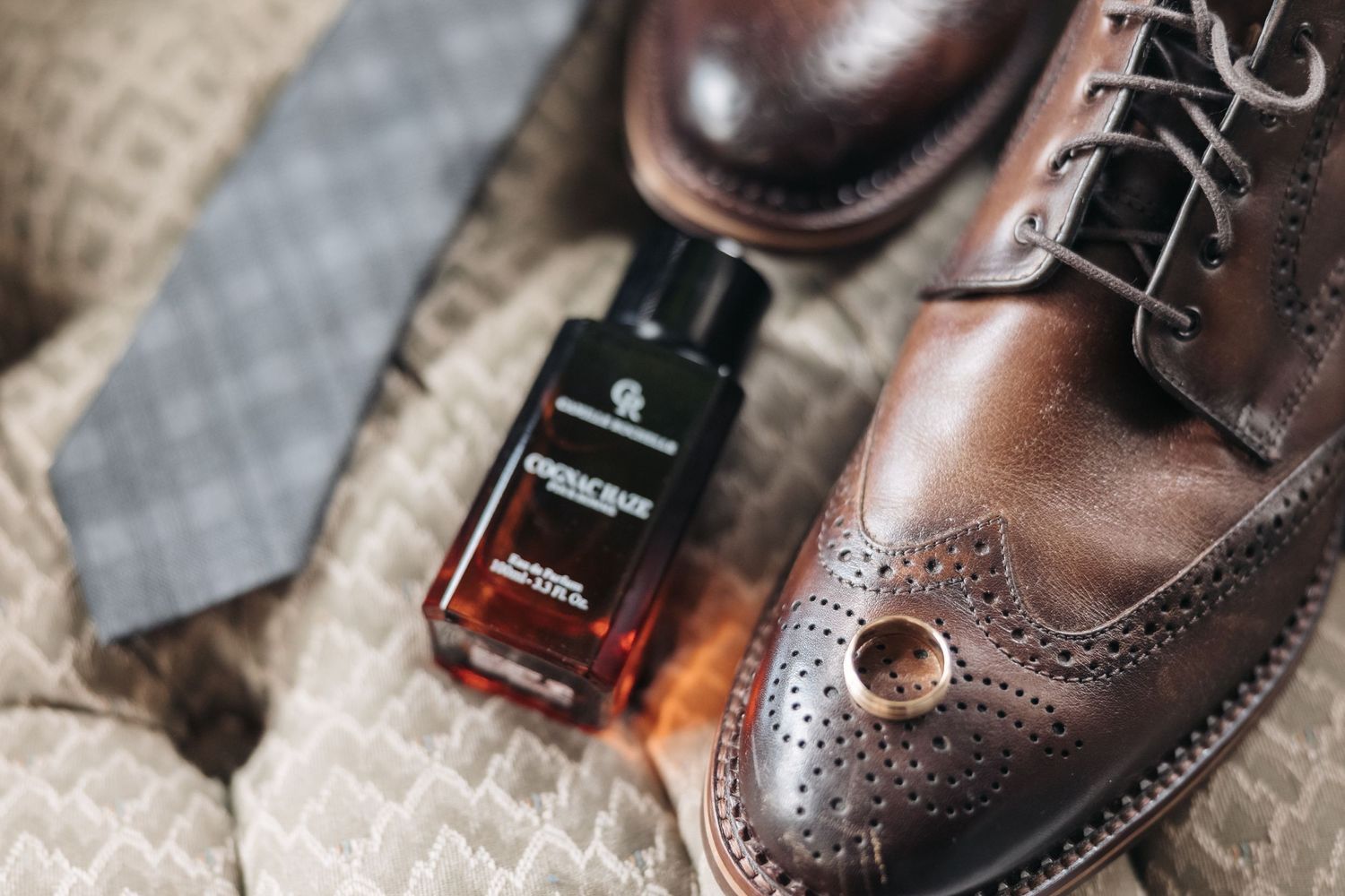 Brown leather brogue dress shoe with cologne bottle and gray necktie.