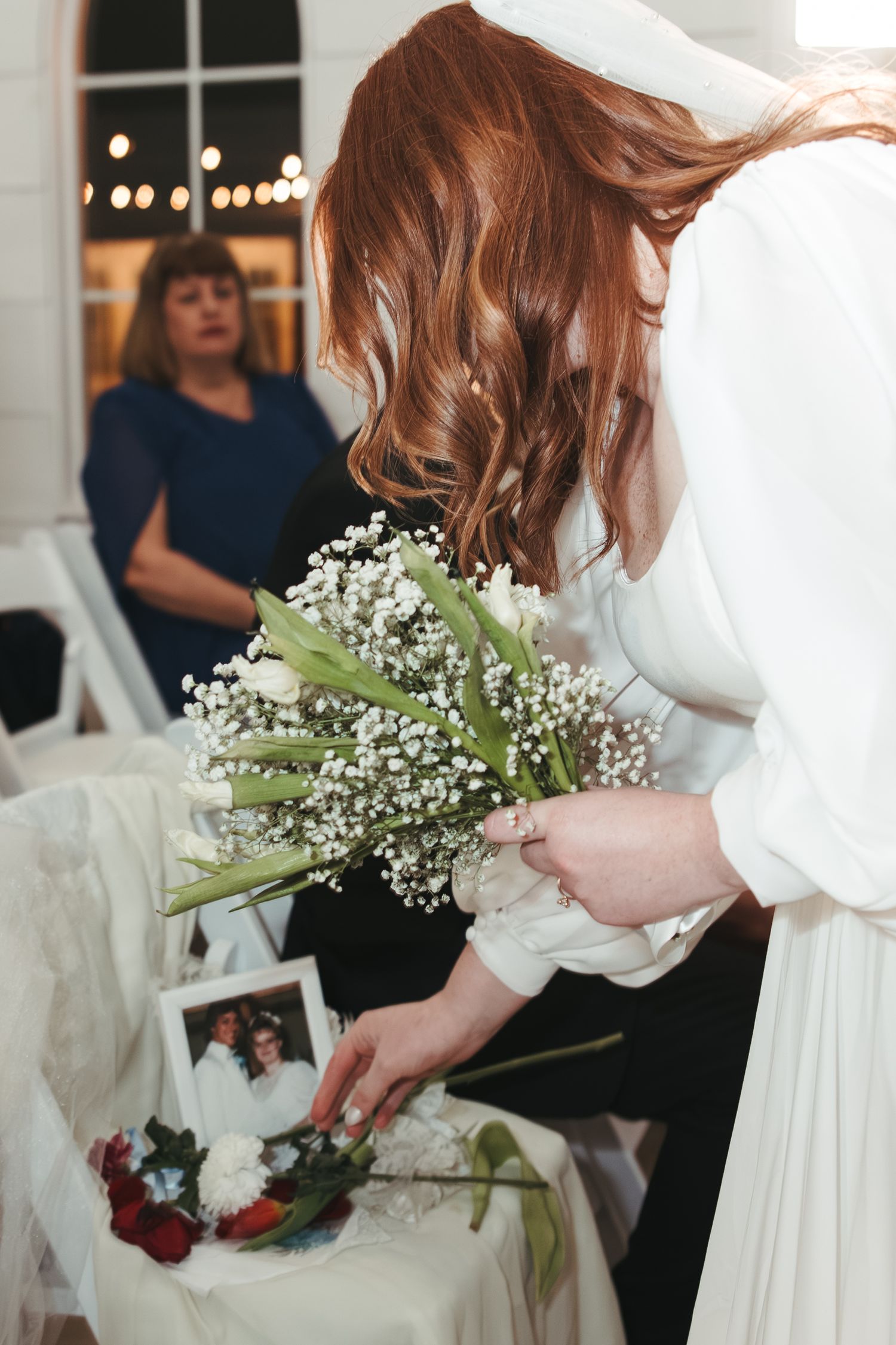 A bride in white holds a bouquet of baby's breath while looking at wedding photos.