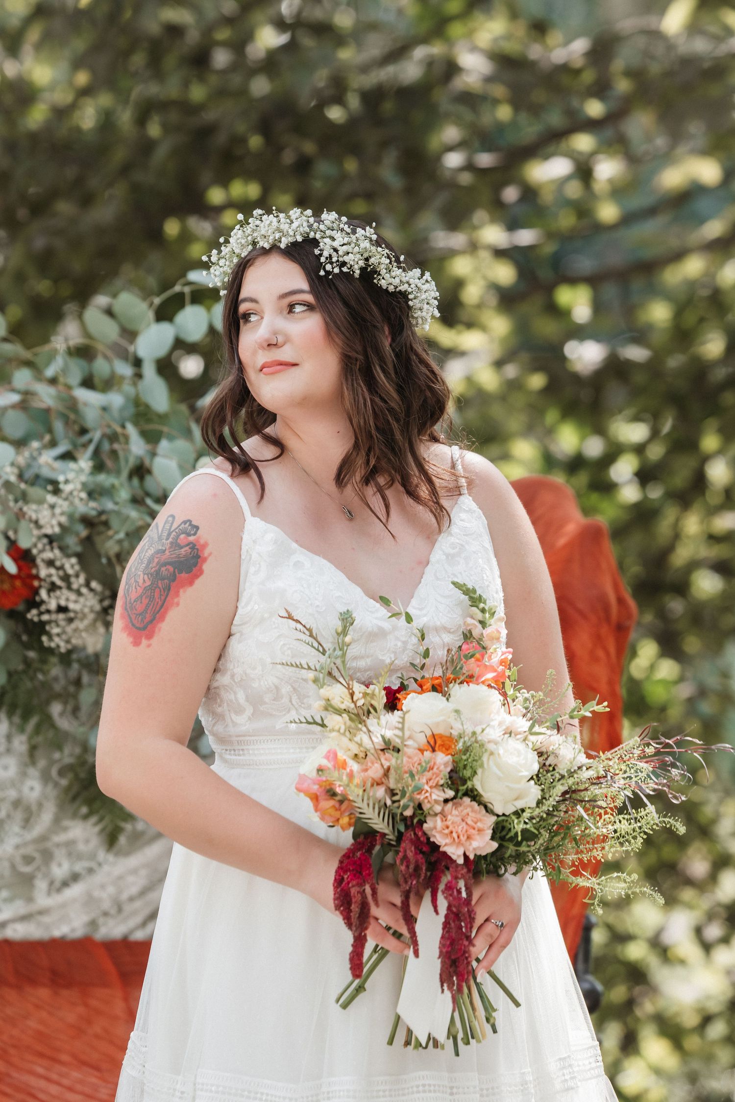 Bride in white dress with floral crown holding colorful bouquet outdoors.
