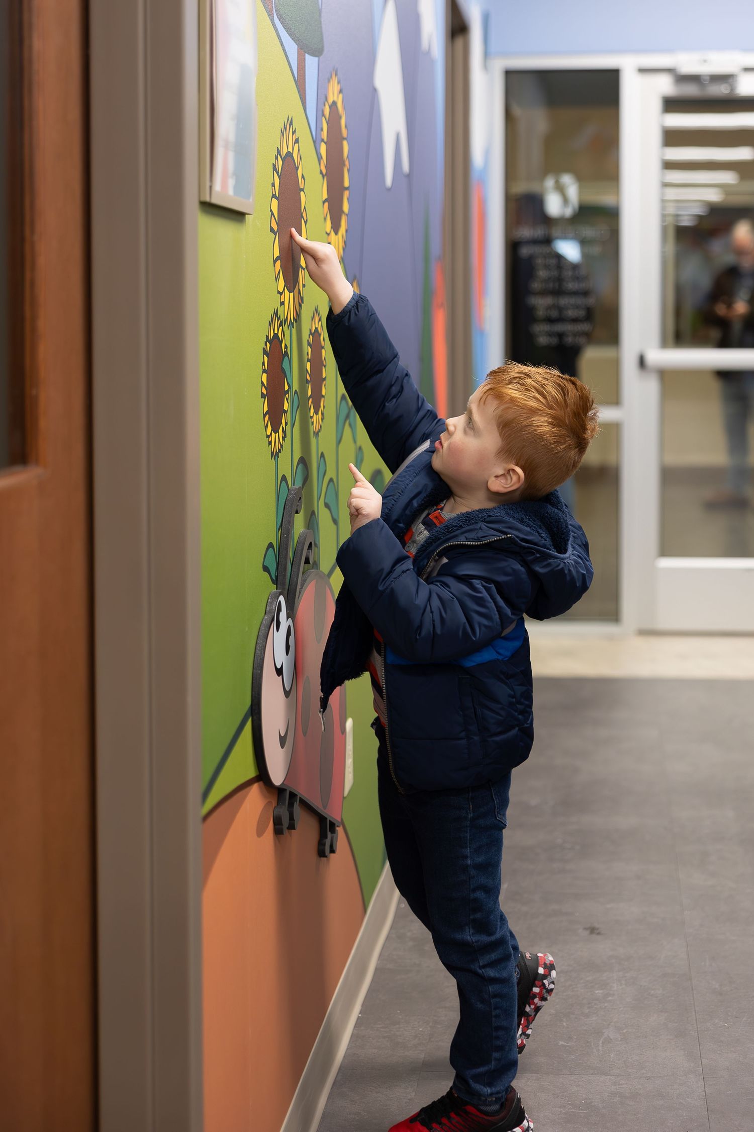 A child in a navy jacket reaches up to touch artwork on a wall.