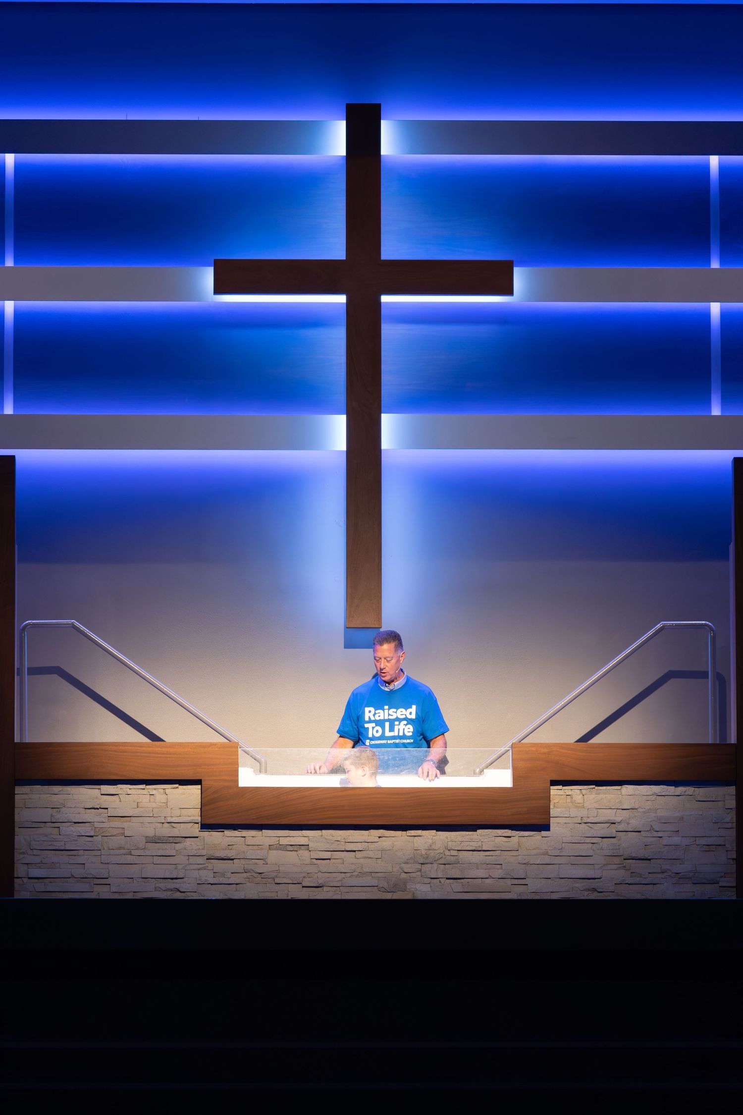 A church stage with illuminated blue lighting and a large cross display in the background.