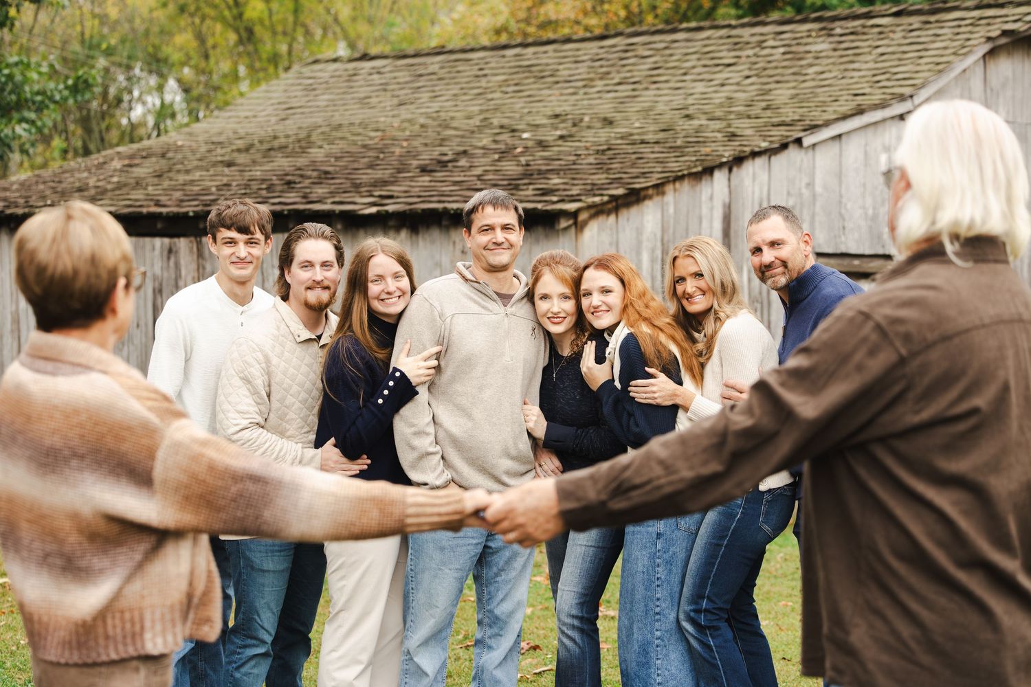 A group of people stand in a line with their arms around each other's shoulders outdoors near a rustic building.