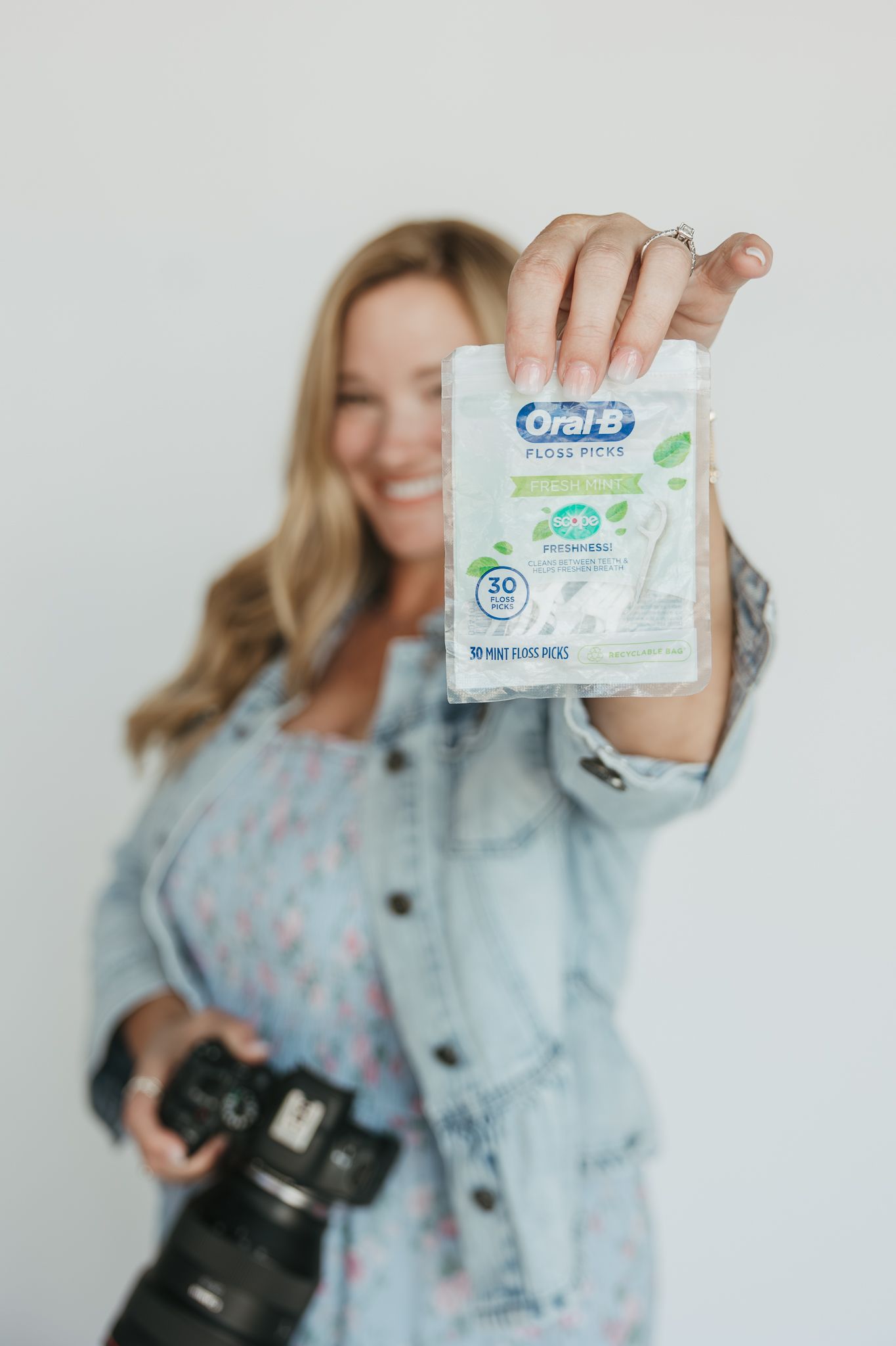 Person in denim jacket holds up Oral-B toothpaste product against white background in promotional photoshoot setting.