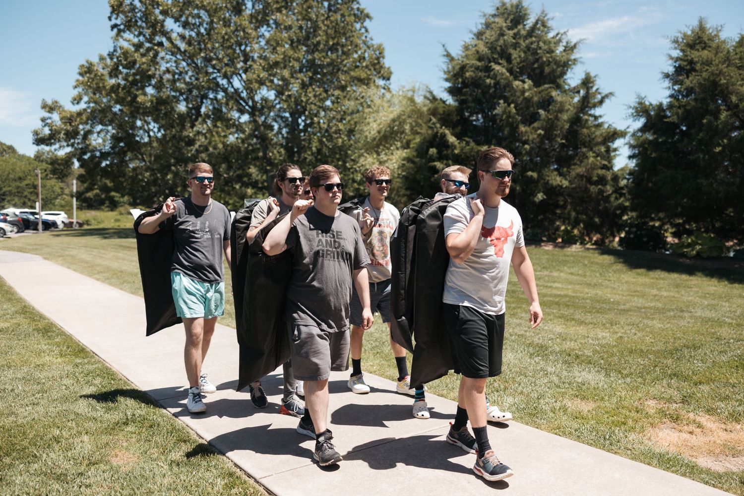 A group walks along a sunny path wearing casual clothes and carrying jackets on a summer day.