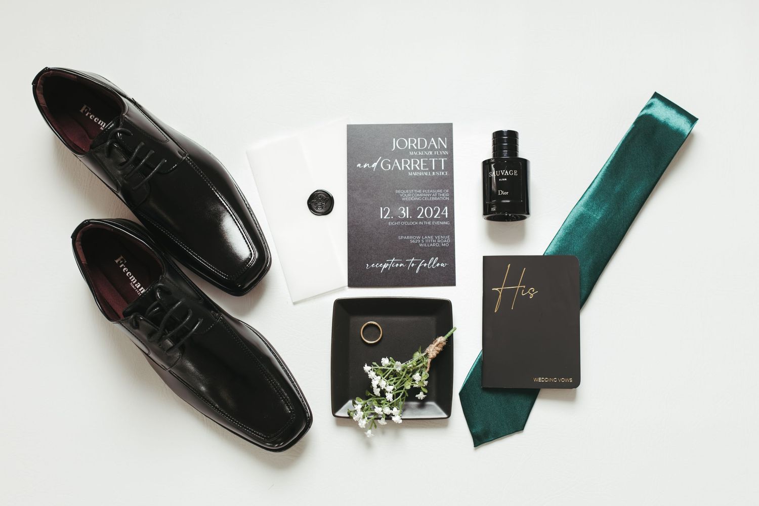 Groom's wedding accessories including black shoes, tie, and invitations on white background.