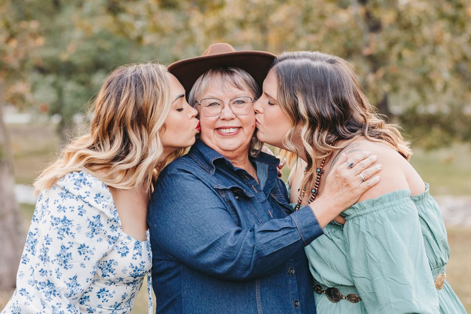 Three women share an affectionate moment together while wearing cowboy hats in a park setting.