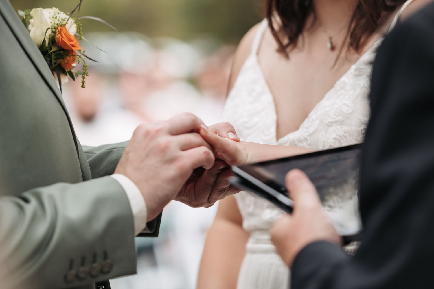 Close-up of wedding ring exchange during outdoor ceremony.