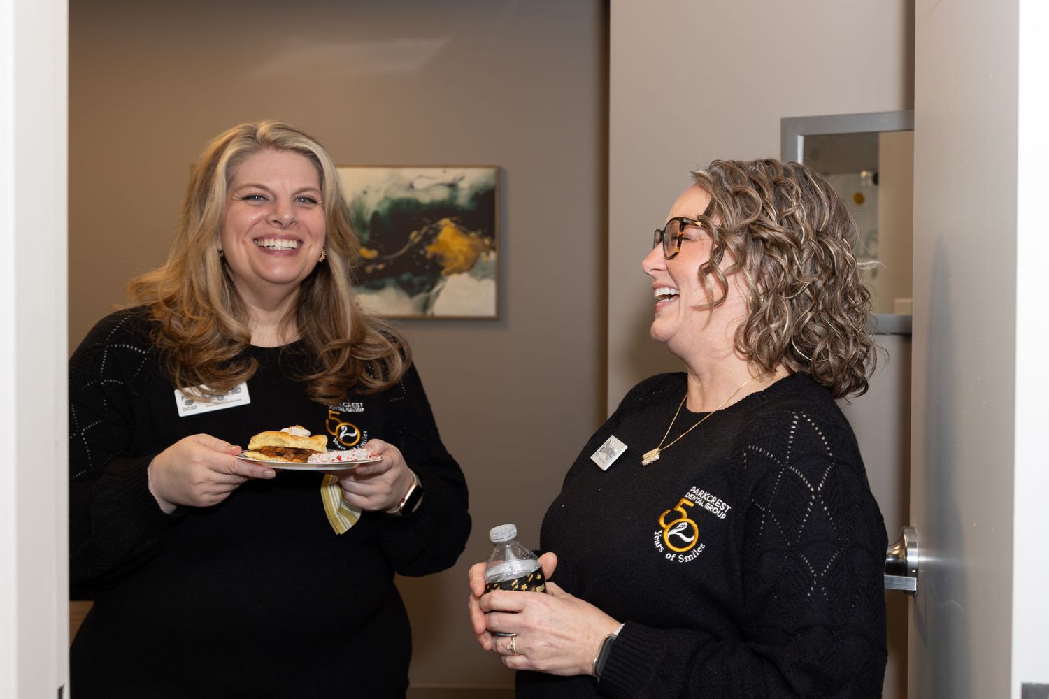 Two staff members in black uniforms sharing refreshments at an office gathering.