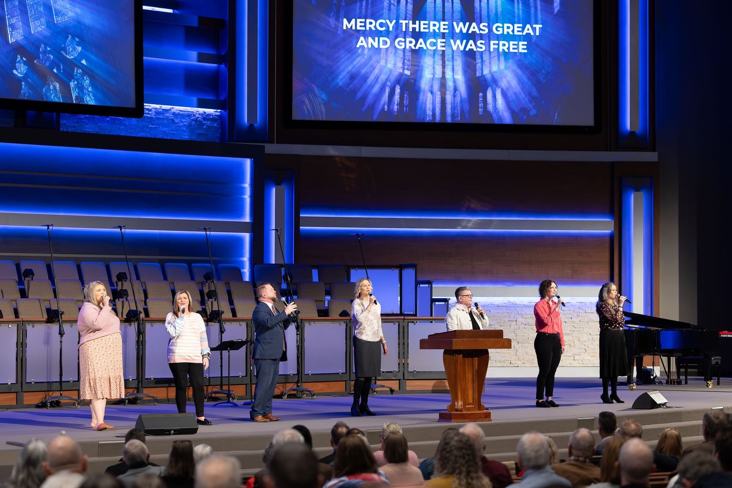 Wide view of church sanctuary during worship service with blue lighting and projection screens.