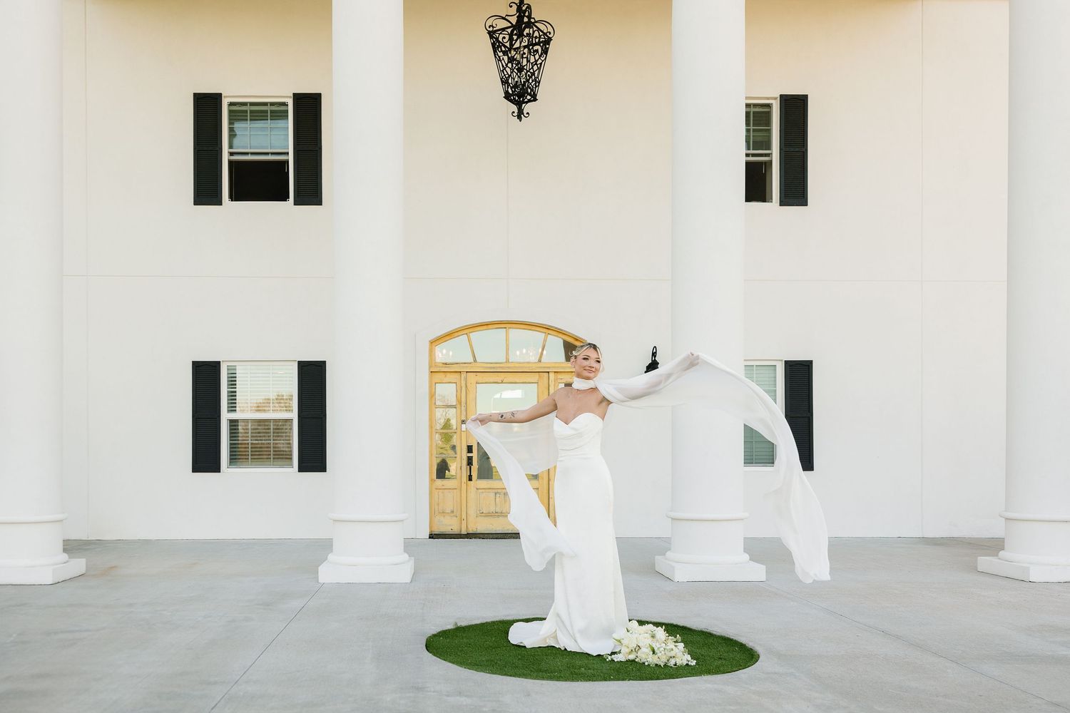 A figure in a flowing white wedding dress twirls elegantly in front of a grand white columned entrance with a golden door.