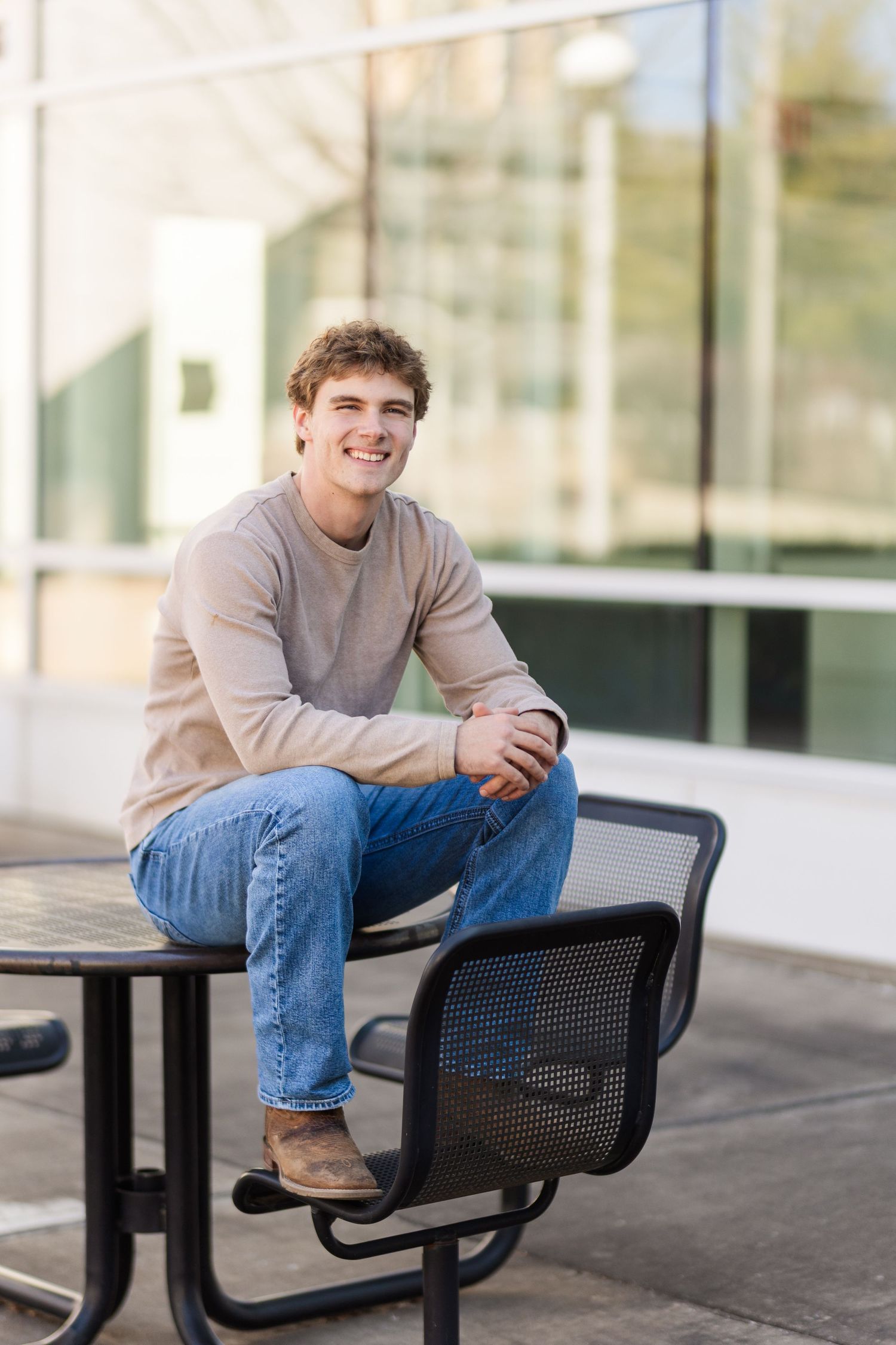 A relaxed portrait of someone in a beige sweater sitting at an outdoor table.