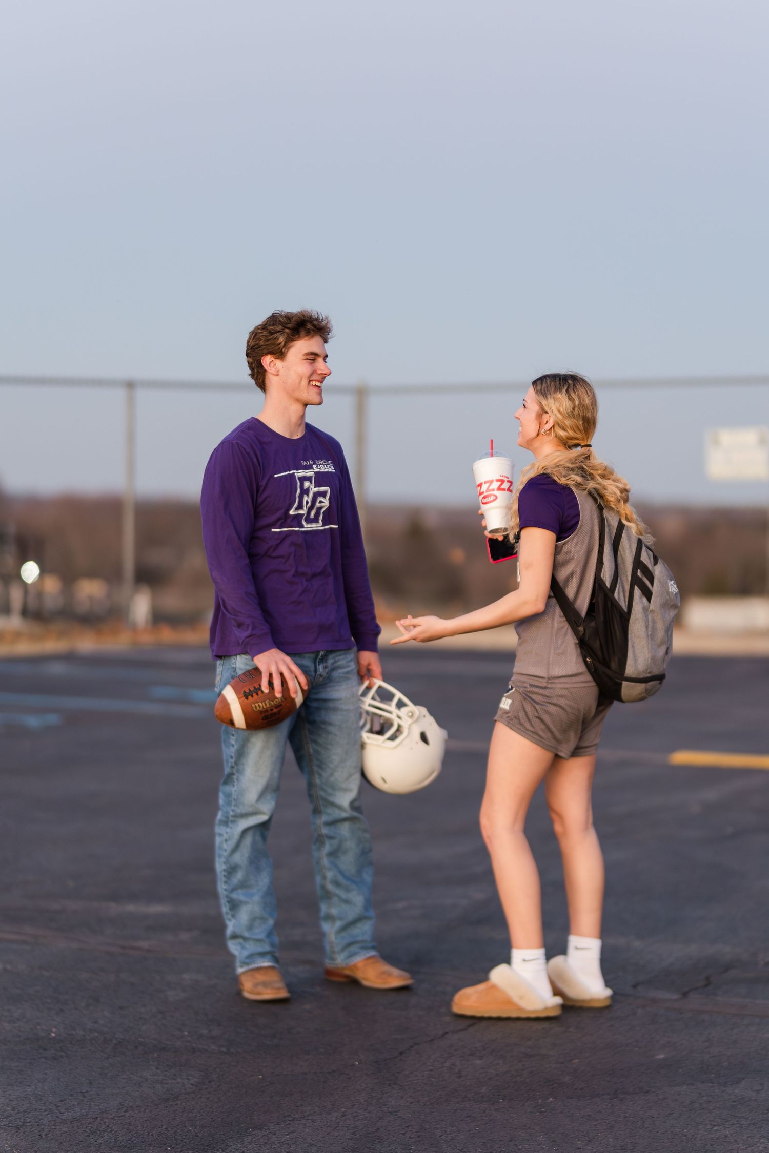 Two students in purple attire chatting outdoors with football and helmet.