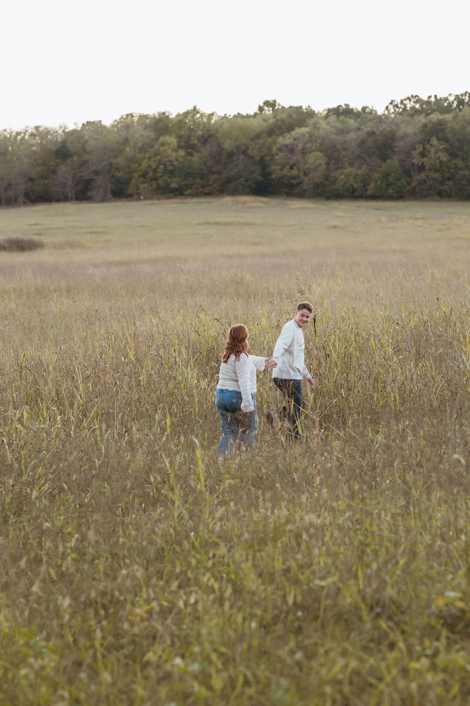Couple holding hands while walking through tall grass in an open field.