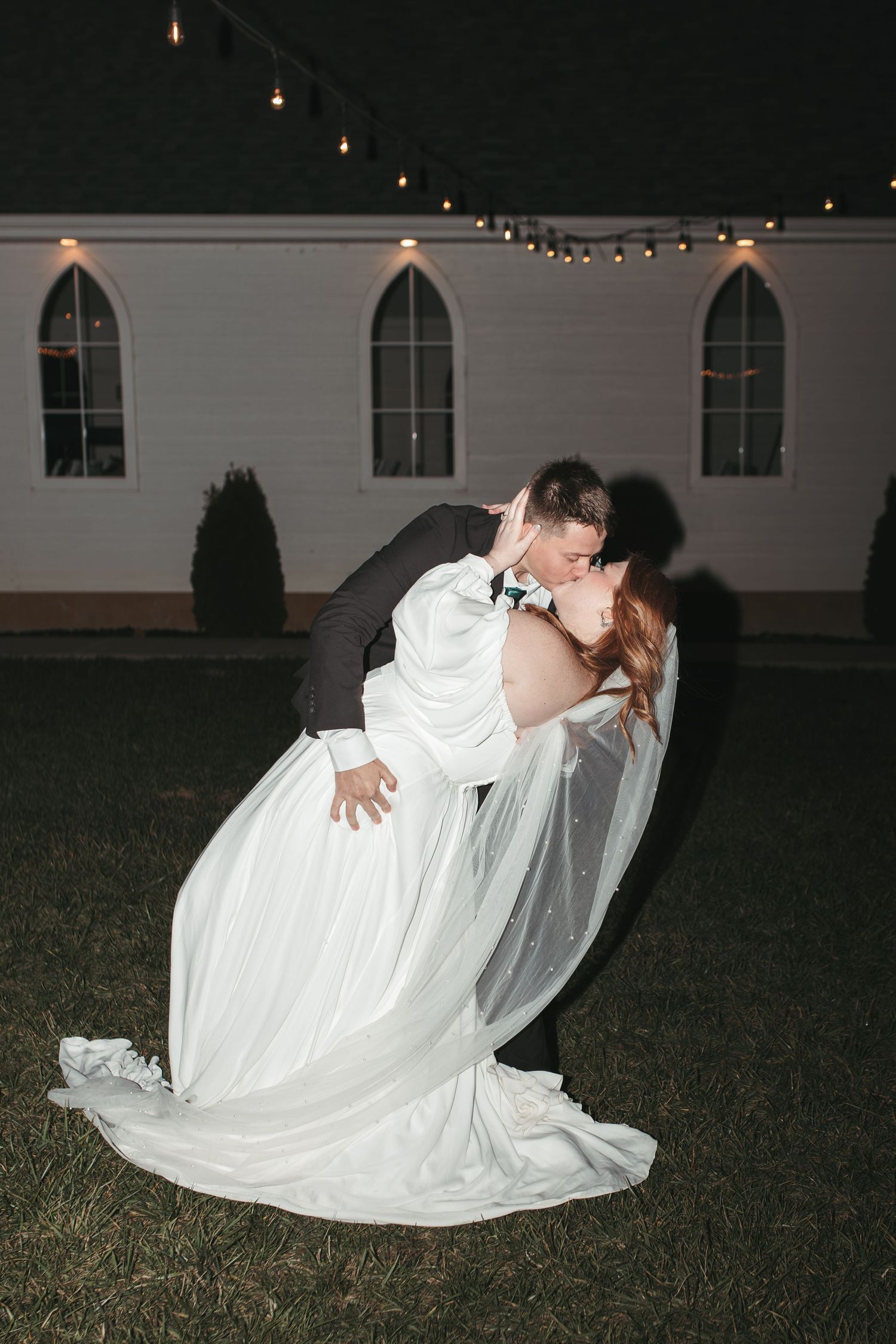 A romantic dip dance pose in front of a white church with string lights.